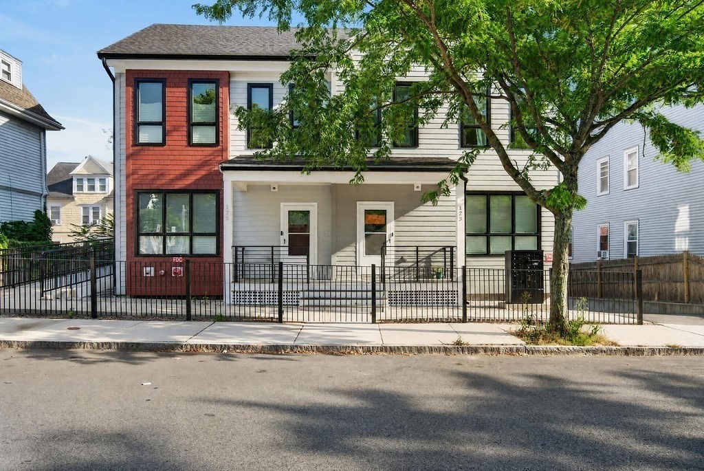 Two-story duplex with red and white siding, fenced front stoops, and a large shade tree.