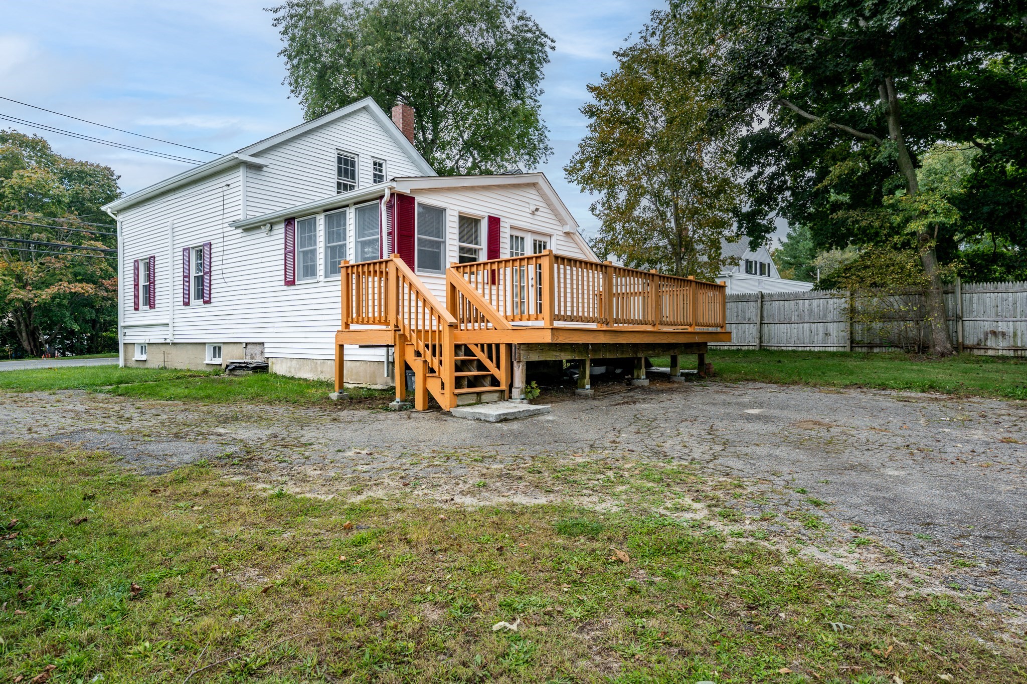 White house with burgundy shutters and a raised wooden deck beside a gravel driveway.