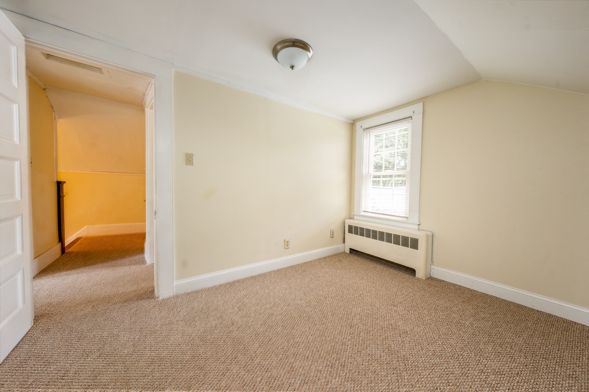 Empty carpeted room with a window, radiator, and open doorway to a hallway.