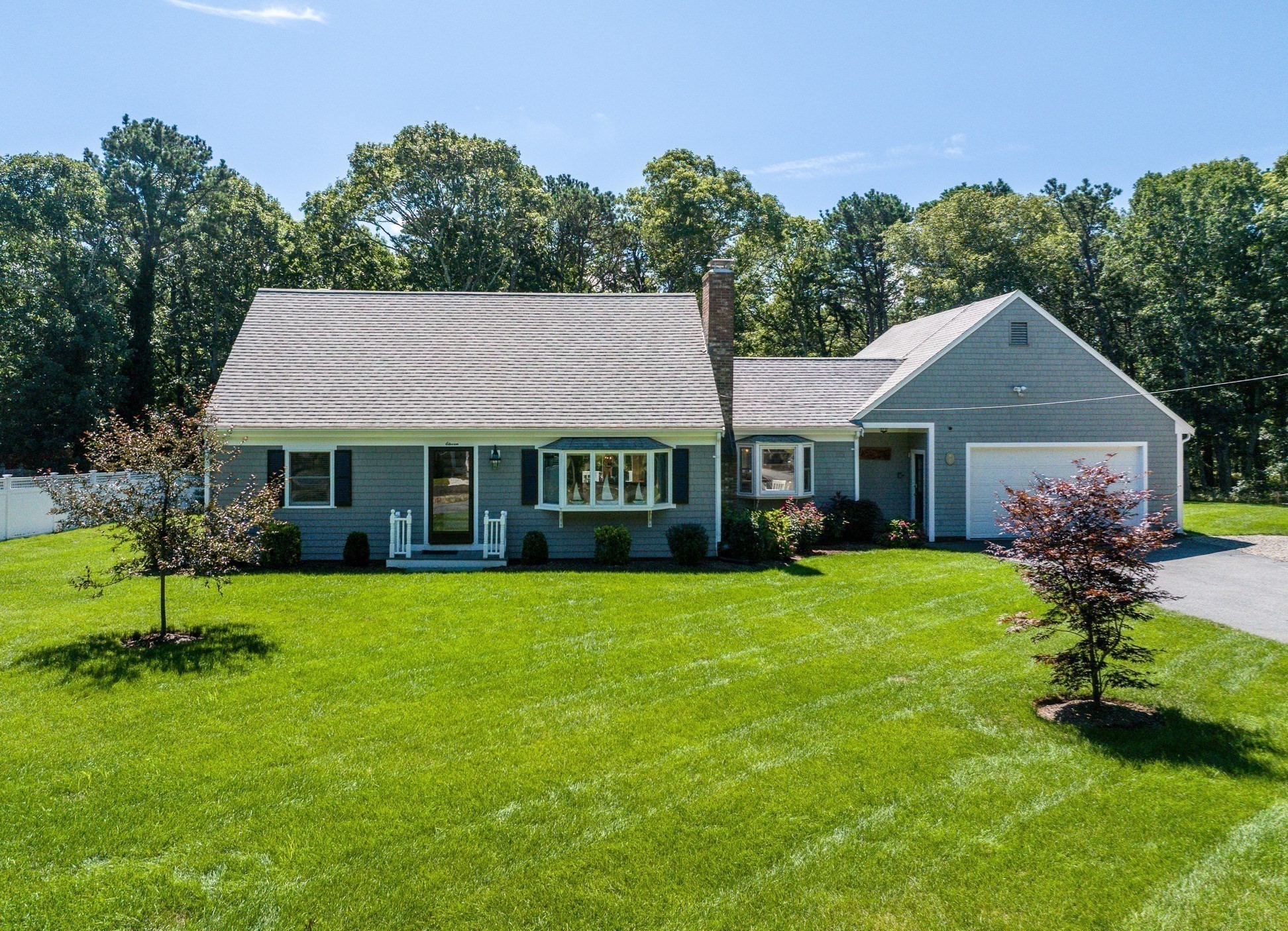 Gray shingle Cape-style home with an attached garage, front bay window, and broad green lawn.