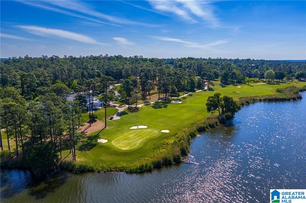 Aerial view of a golf course and lake bordered by pine trees.