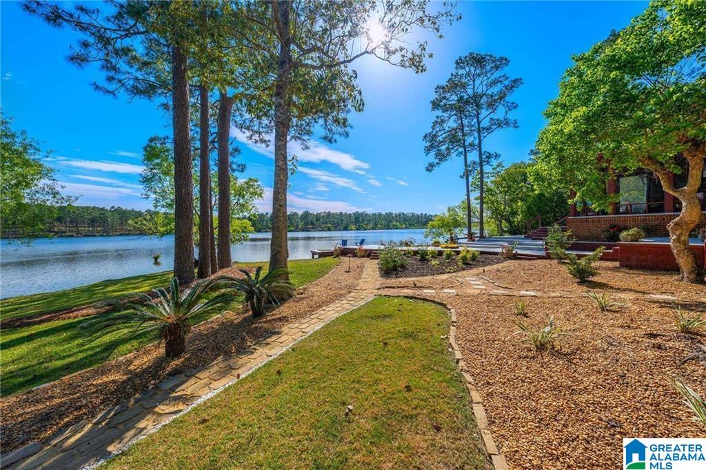 Lakefront backyard with mature trees, a curved stone path, and landscaped garden beside the water.