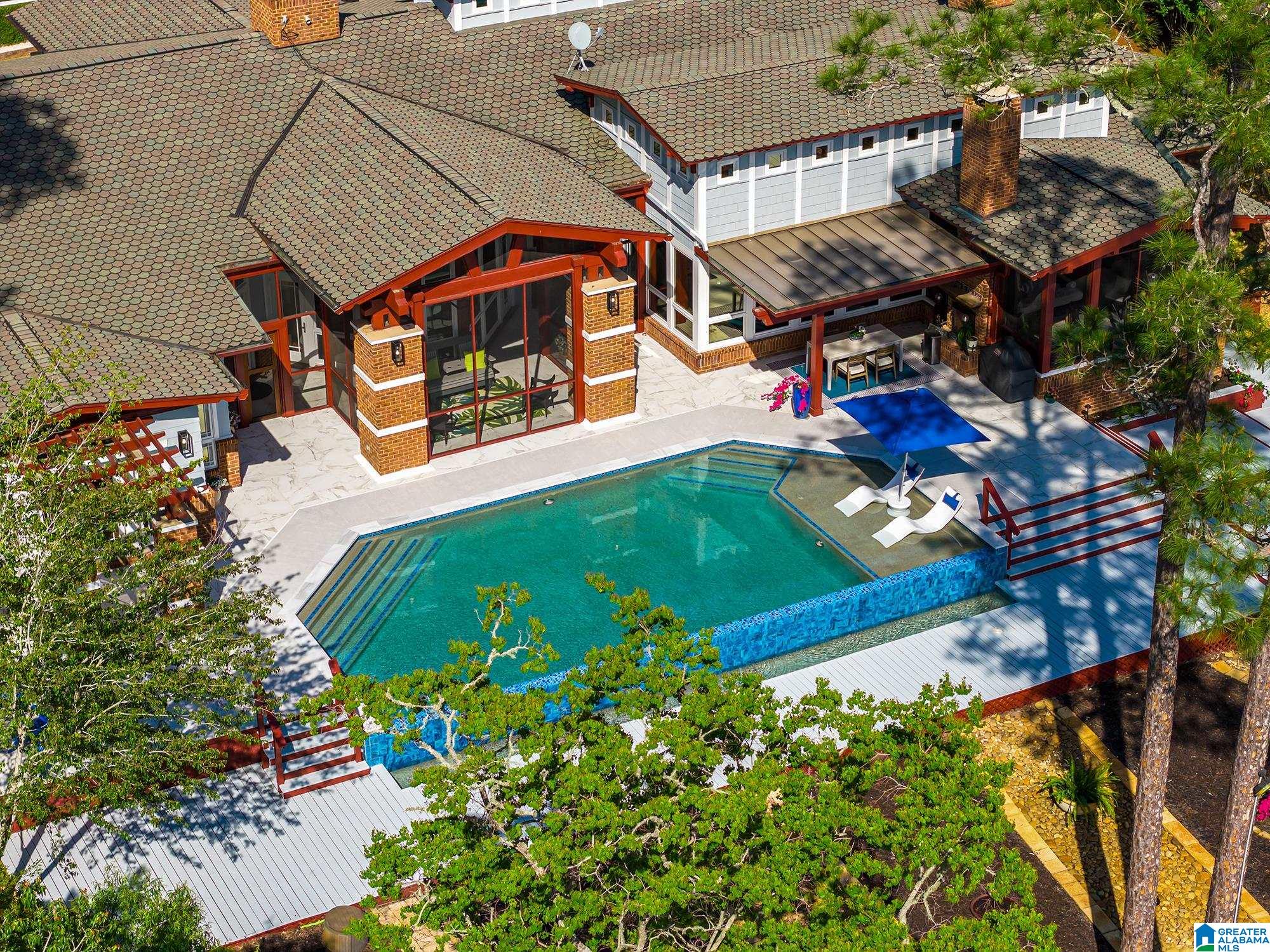 Aerial view of a home with a turquoise pool, broad steps, and a covered patio.