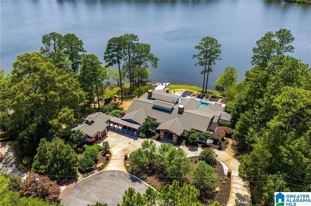 Aerial view of a large home on the water, surrounded by mature trees and landscaped grounds.