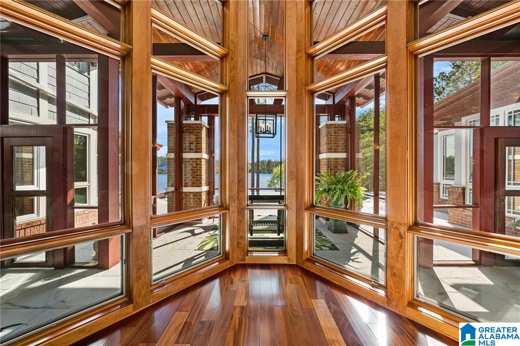 Sunroom with warm wood-framed windows overlooking a lake and patio.