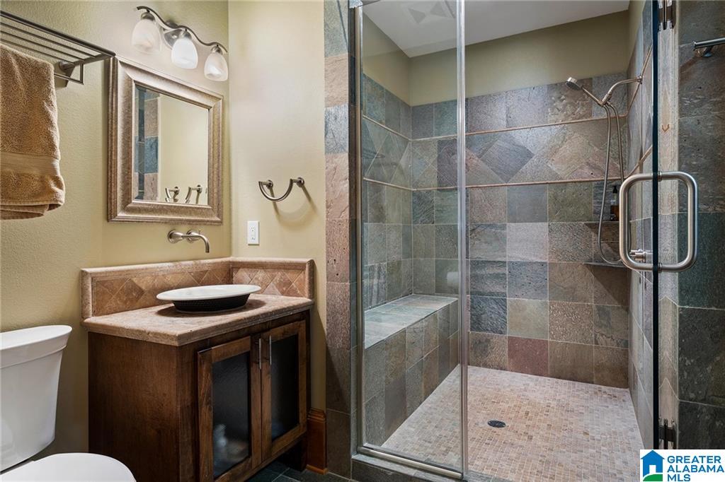 Bathroom with a multicolored stone-tile walk-in shower, built-in bench, and wood vanity with vessel sink.