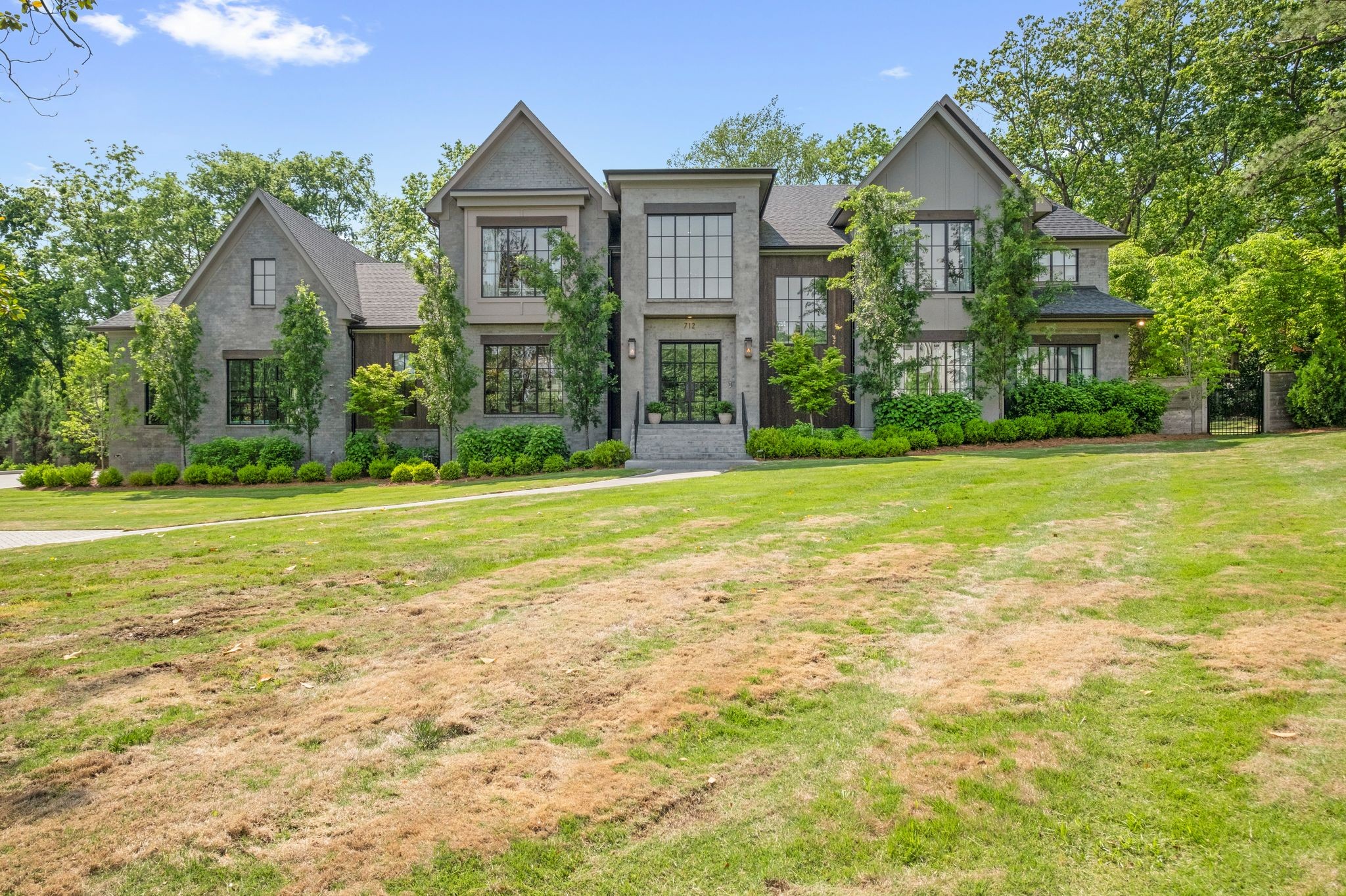 Large gray home with peaked rooflines, black-framed windows, and a broad front lawn.