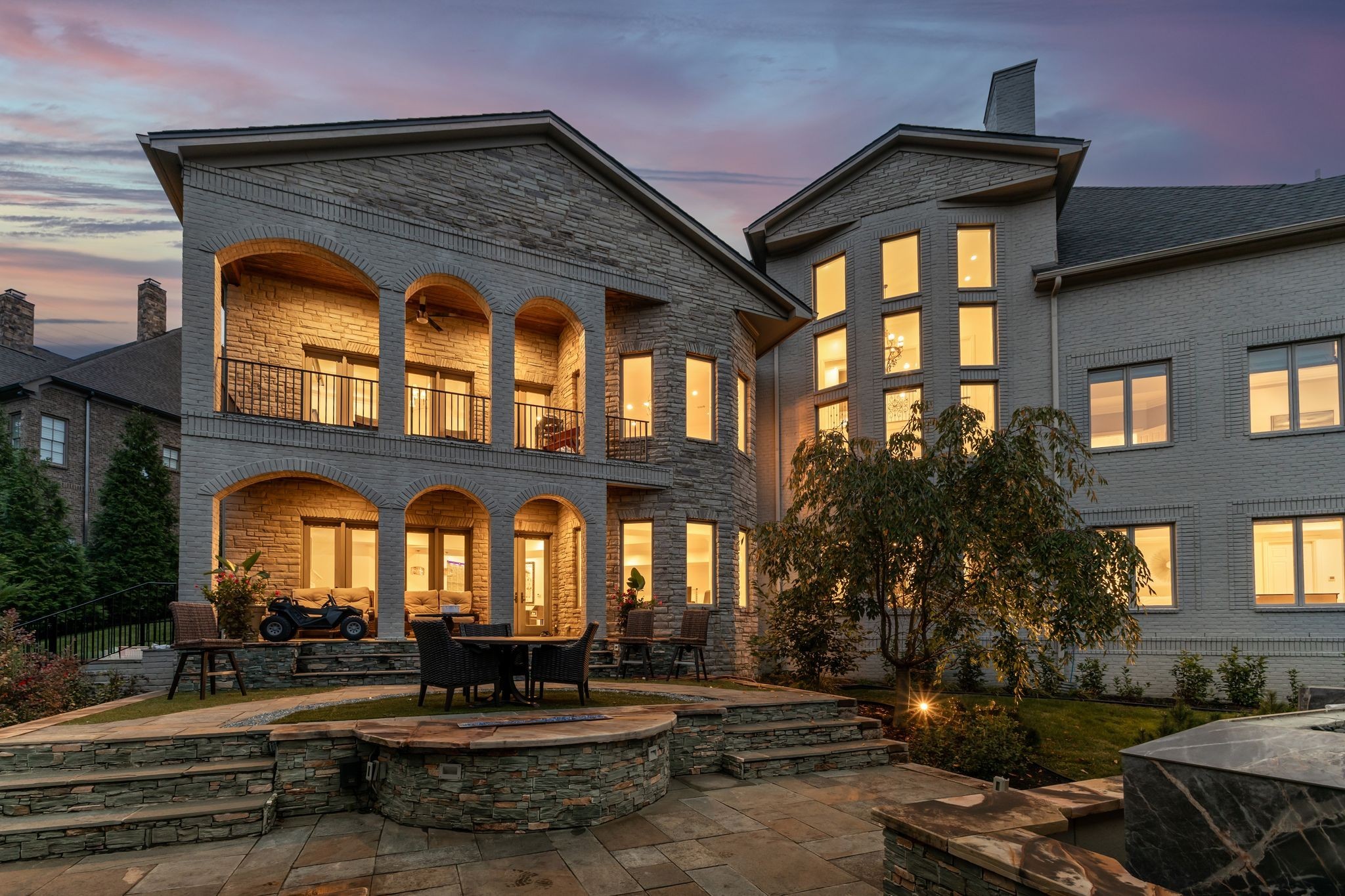 Stone home at dusk with arched balconies and a tiered patio with outdoor seating.