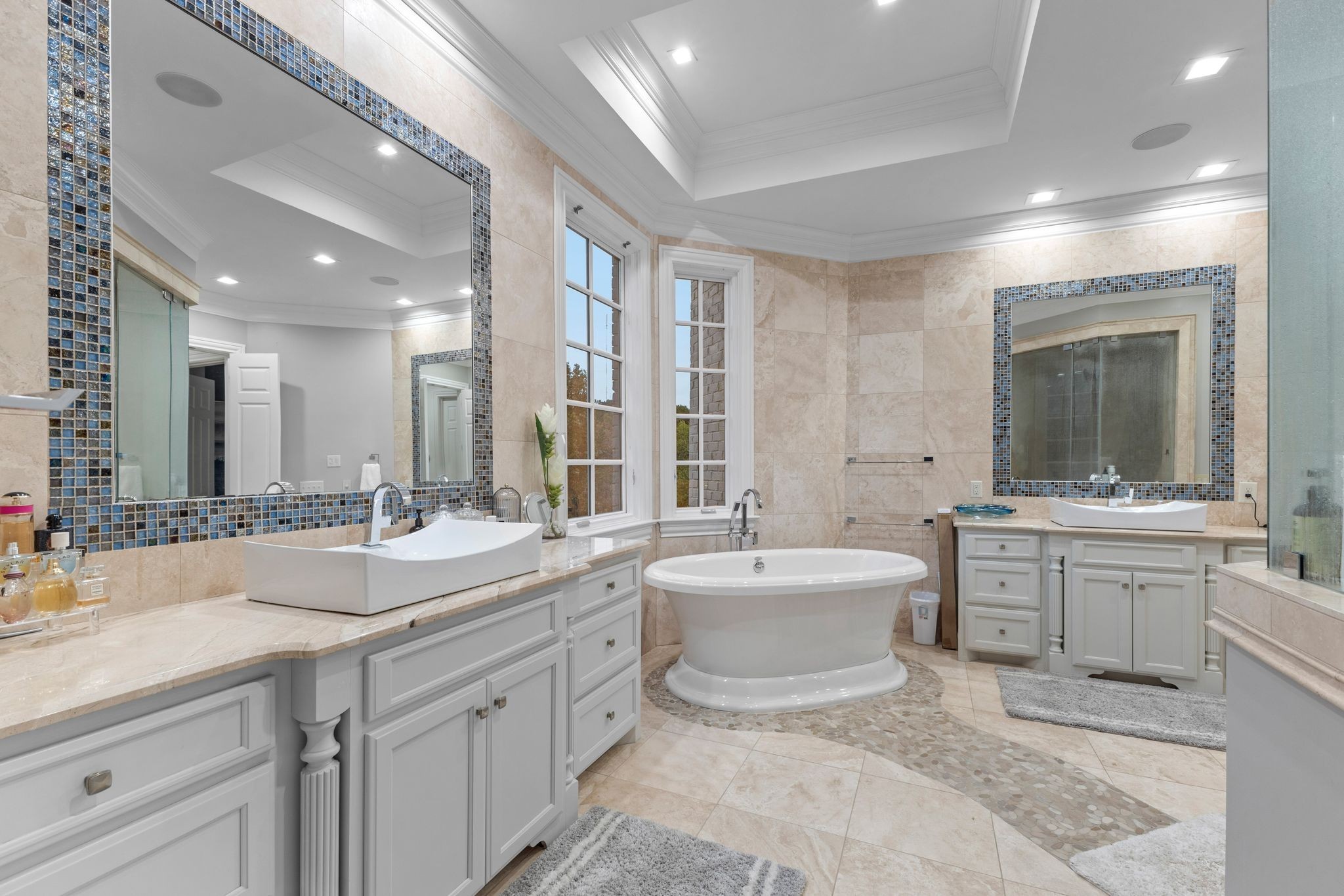 Primary bathroom with freestanding tub, double vanities, and blue mosaic-trimmed mirrors.