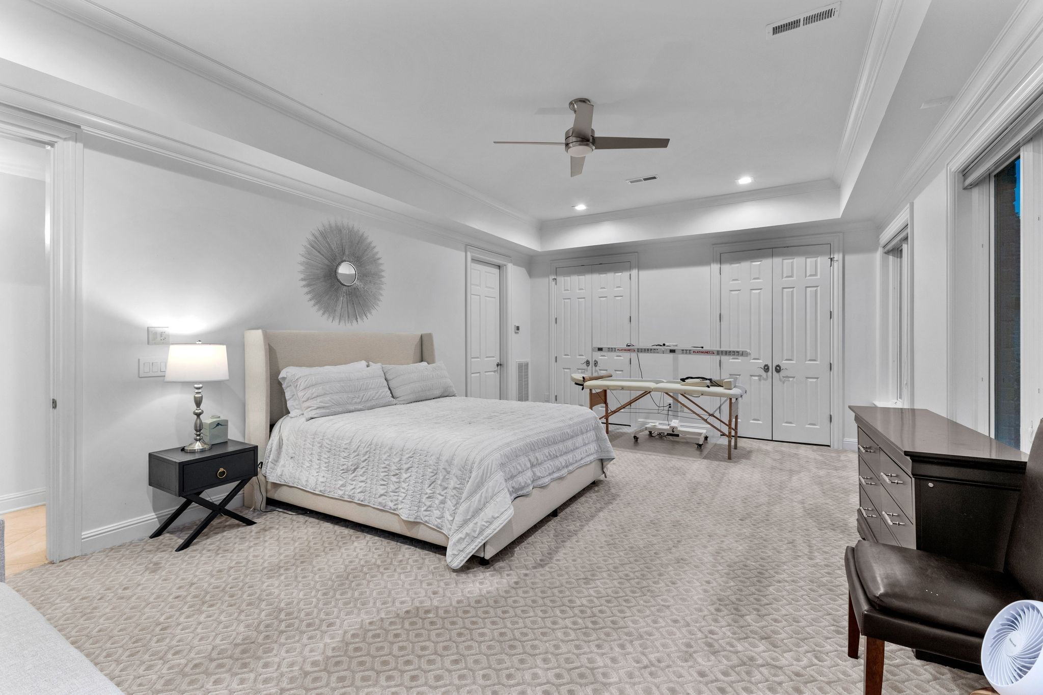 Furnished bedroom with a large bed, patterned carpet, and ironing board by the closet doors.