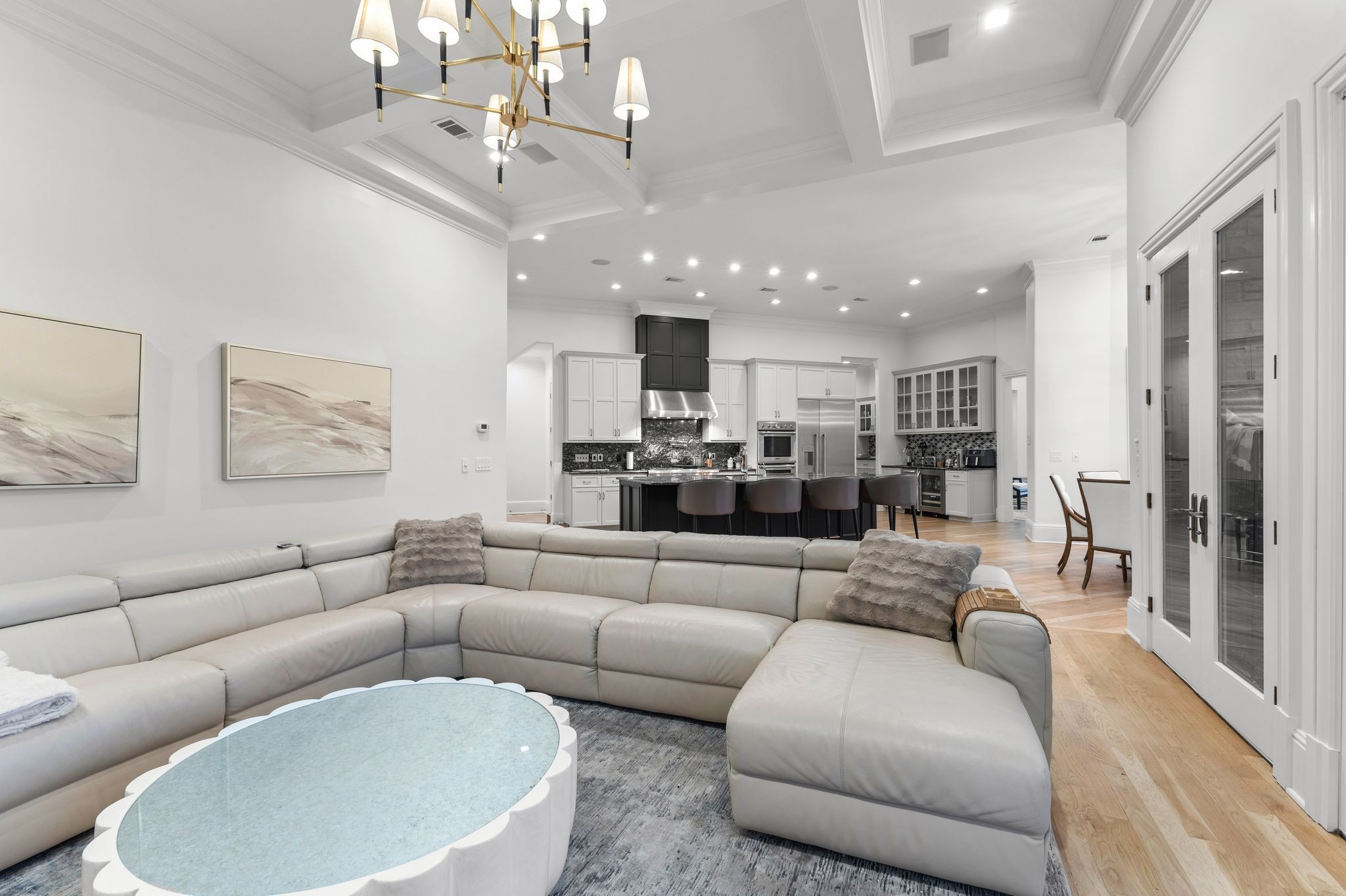 Furnished living room with a large sectional sofa opening onto a white-and-dark kitchen.