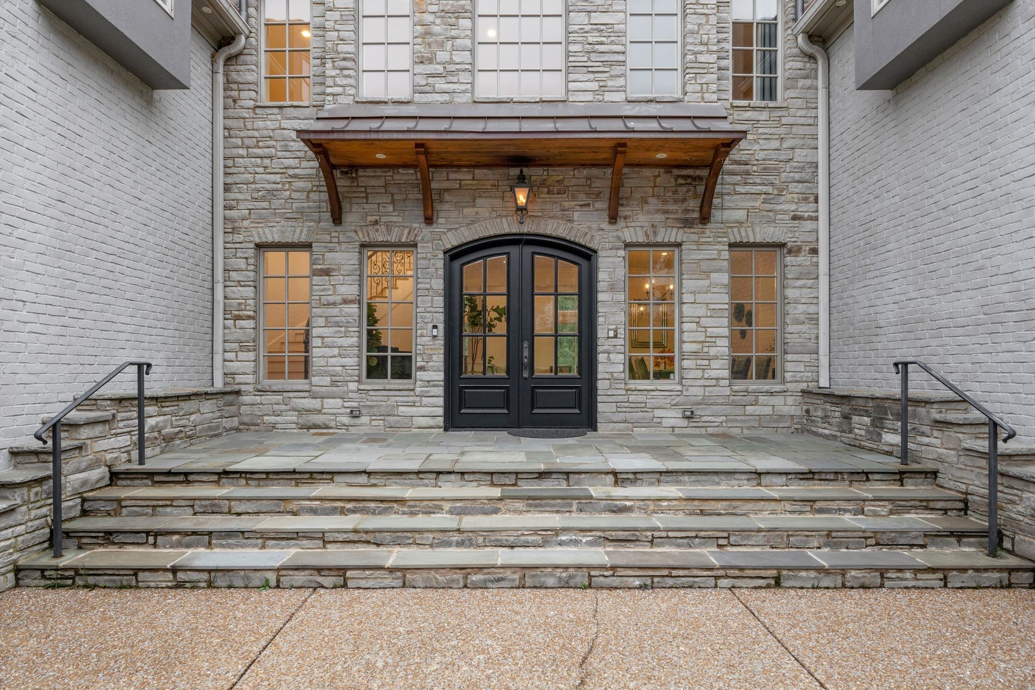 Stone home entrance with arched black doors, a timber canopy, and broad stone steps.
