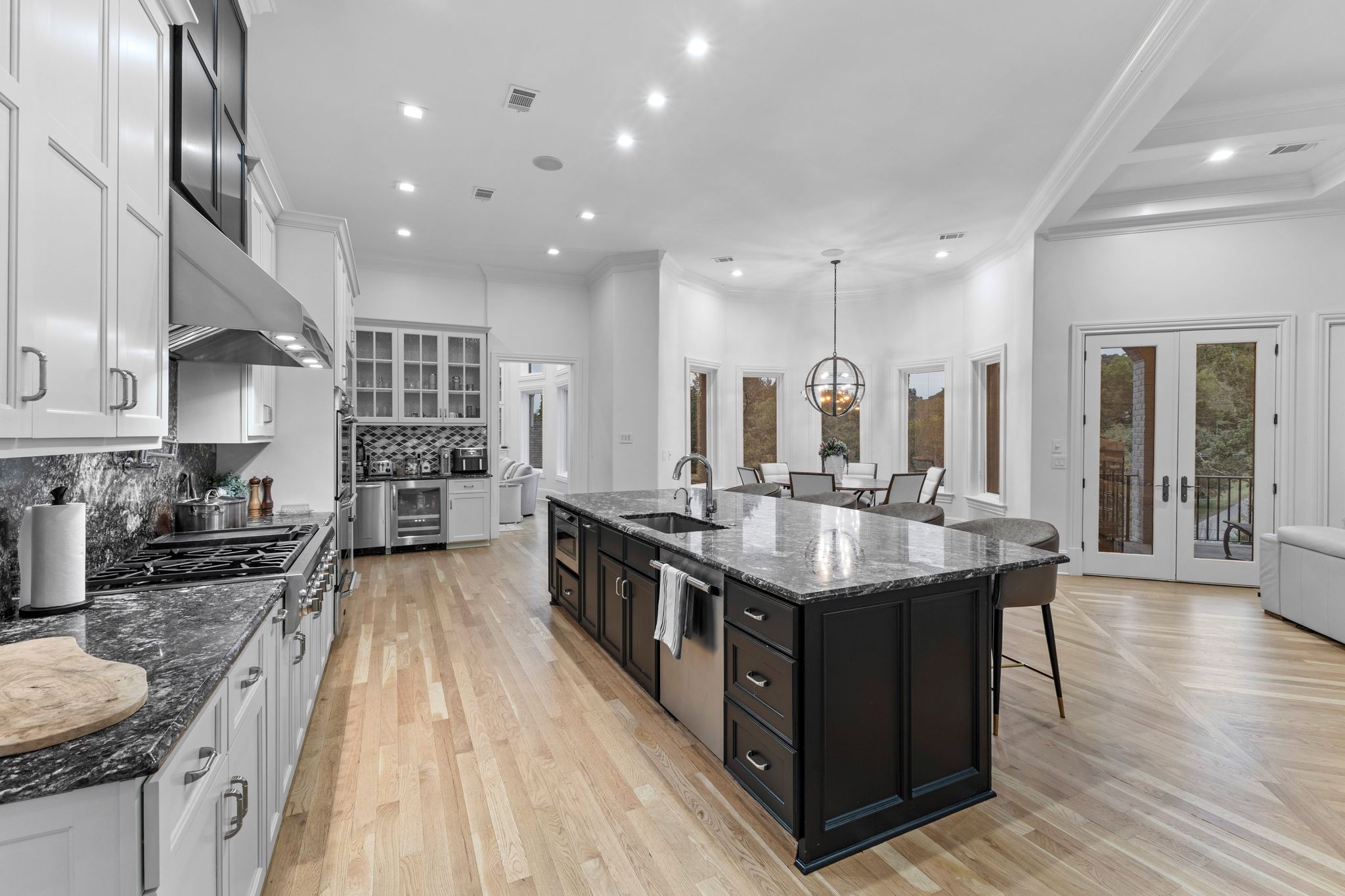 Kitchen with a large dark island, stone counters, white cabinets, and adjoining dining area with deck doors.