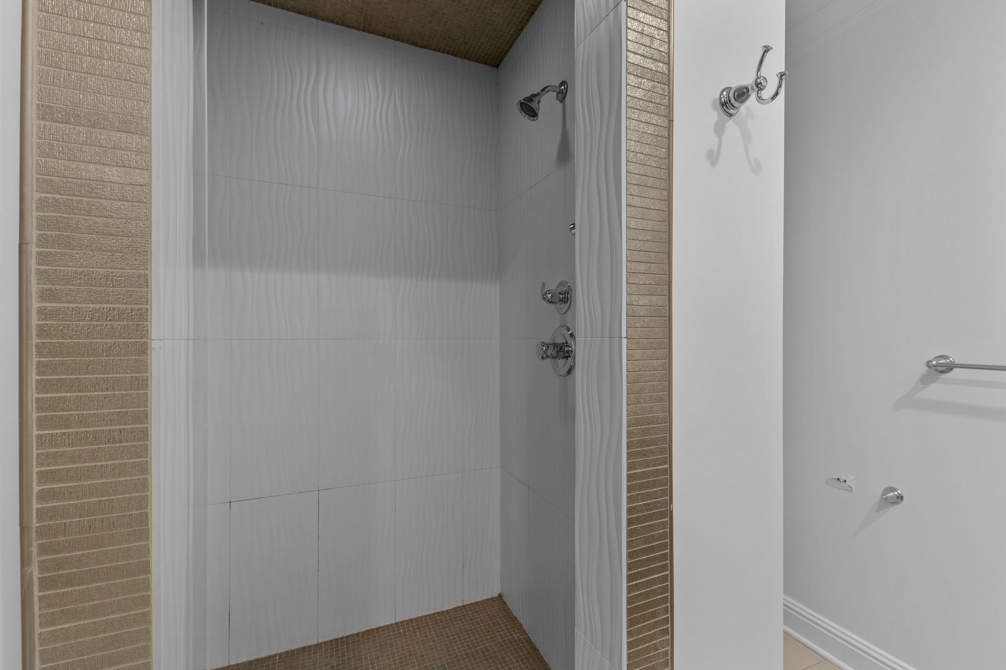 Bathroom shower with white wavy tiles, tan tile borders, and chrome fixtures.