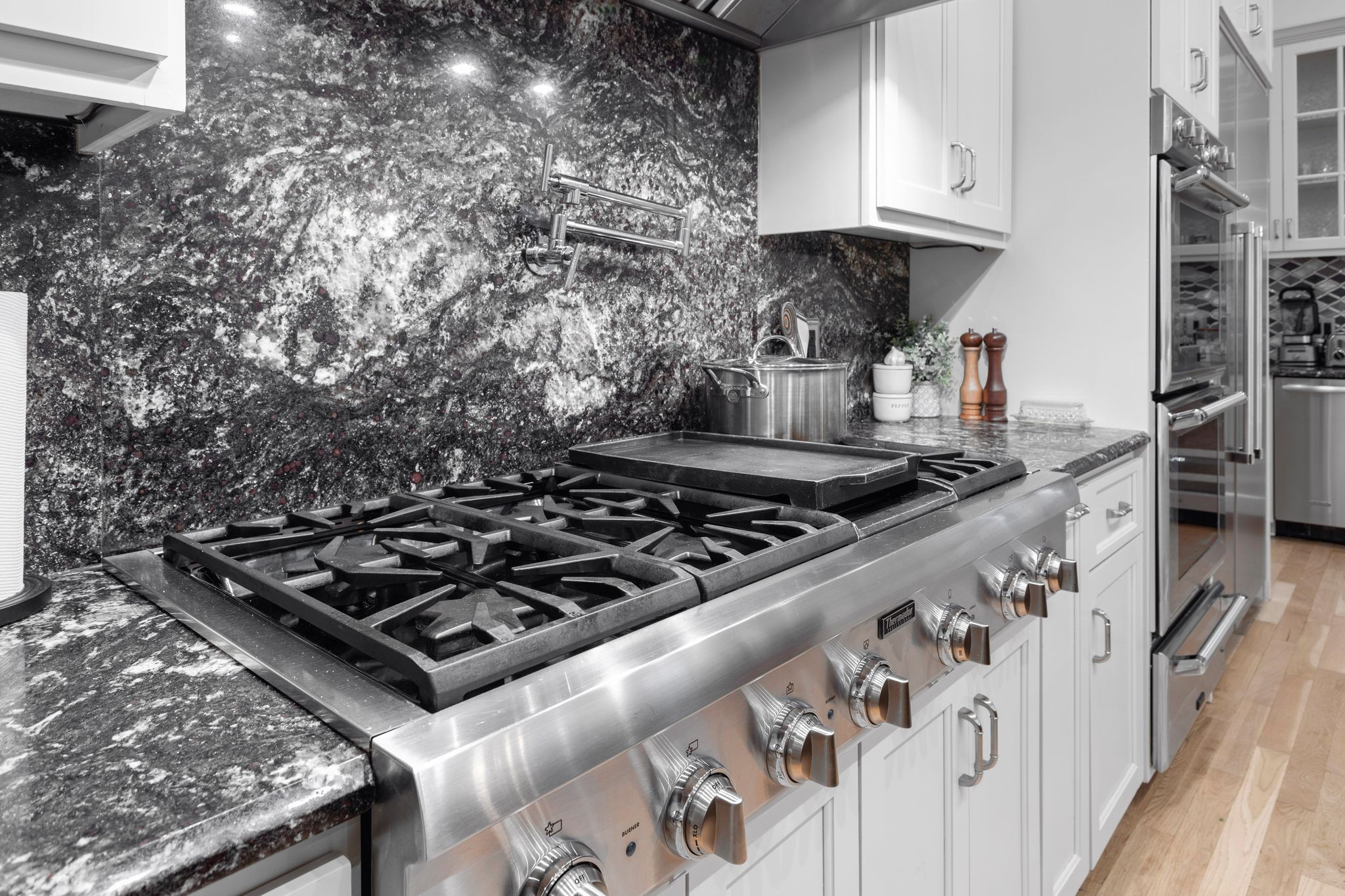 Kitchen with a stainless-steel commercial-style range, dark granite backsplash, and white cabinetry.