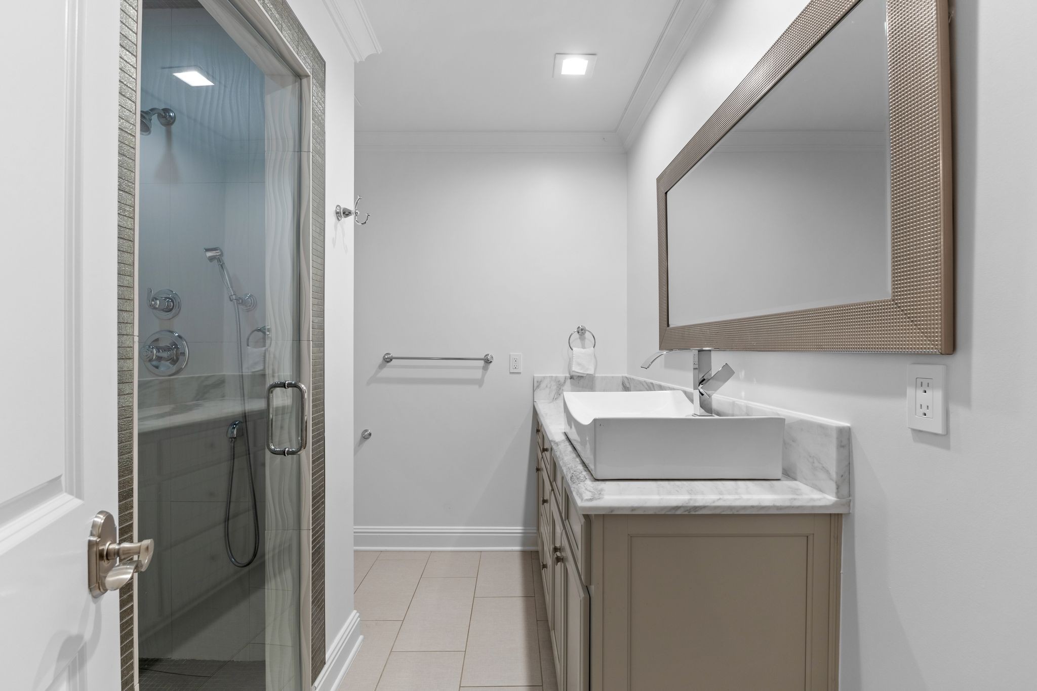 Bathroom with glass shower and vessel sink on a marble-topped vanity.