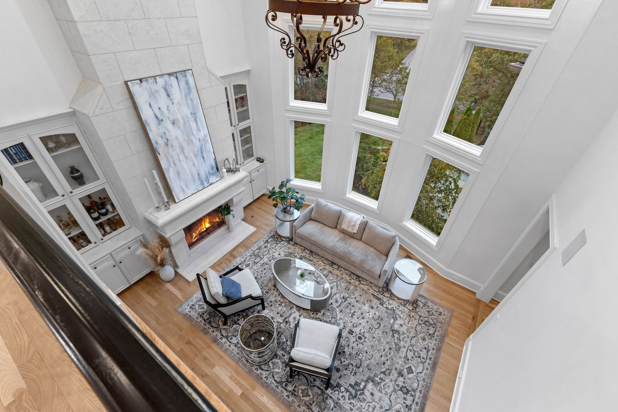 Furnished living room with a tall window wall, white stone fireplace, and patterned rug.
