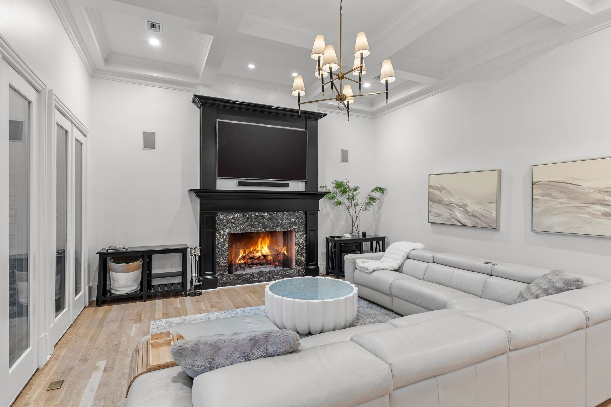 Living room with a white sectional, round coffee table, and lit fireplace beneath a mounted television.