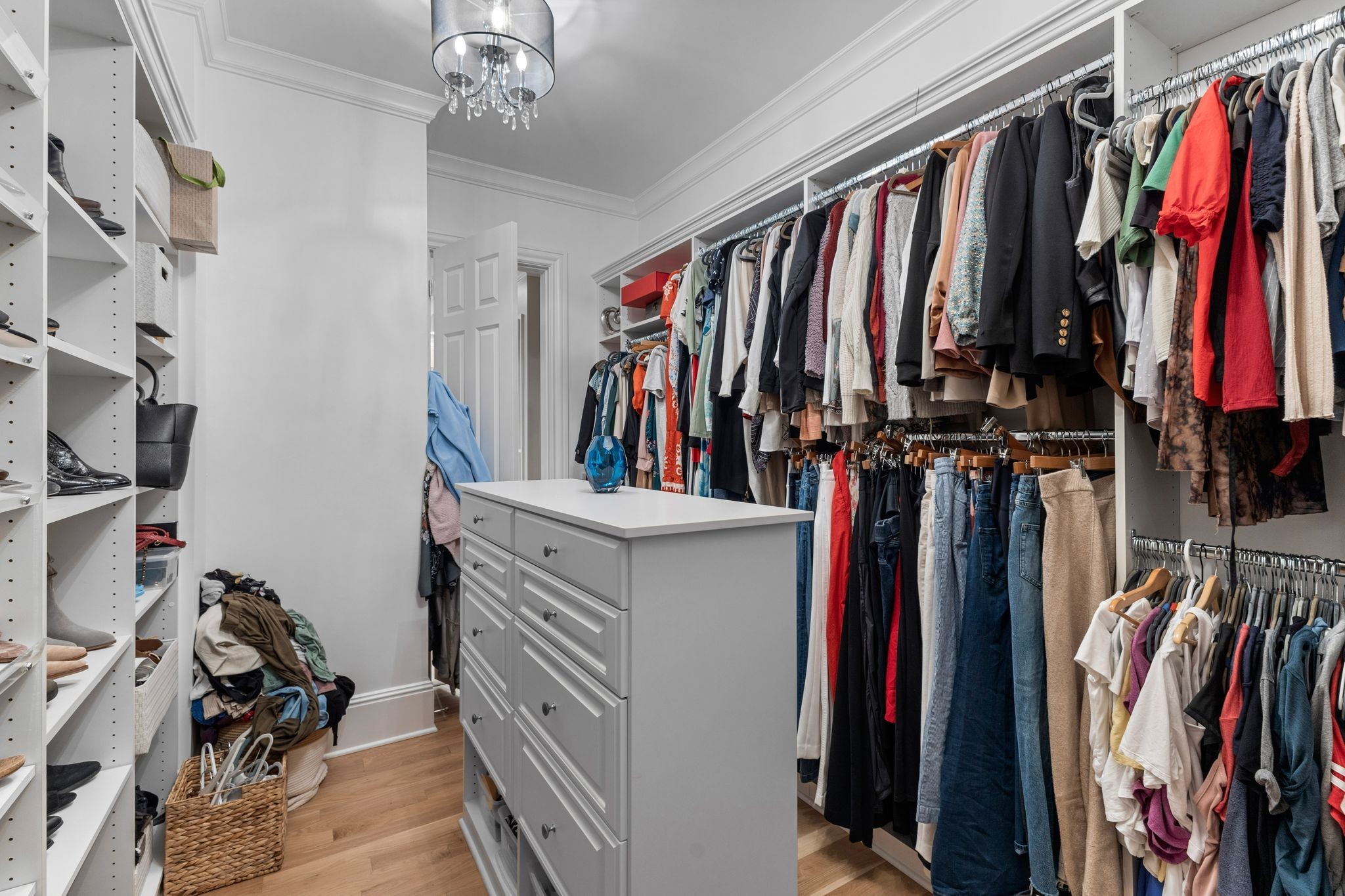 Walk-in closet with a central drawer island, built-in shoe shelves, and clothing racks filled with clothes.
