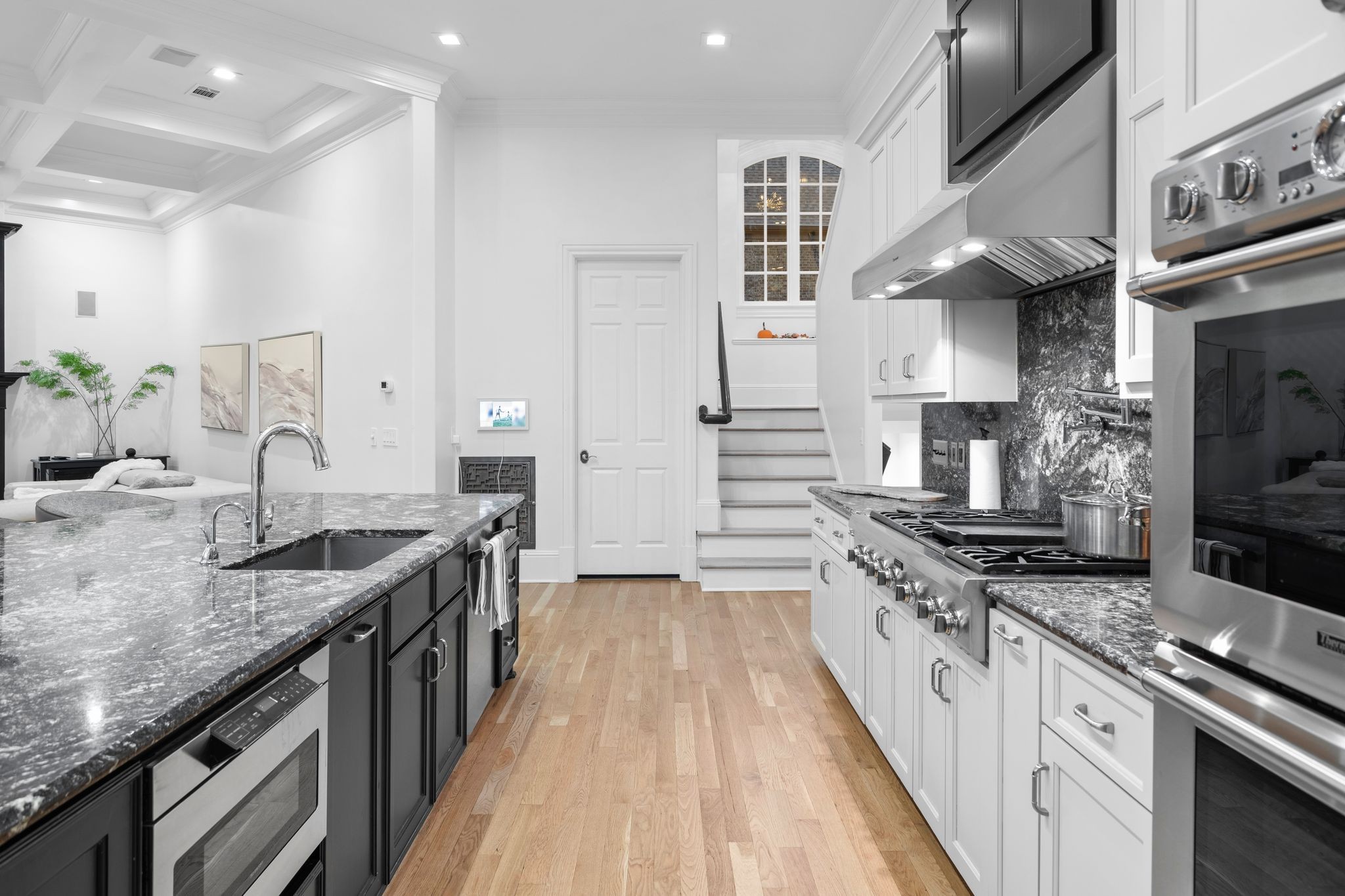 Kitchen with a large stone island, stainless steel appliances, and a staircase behind it.