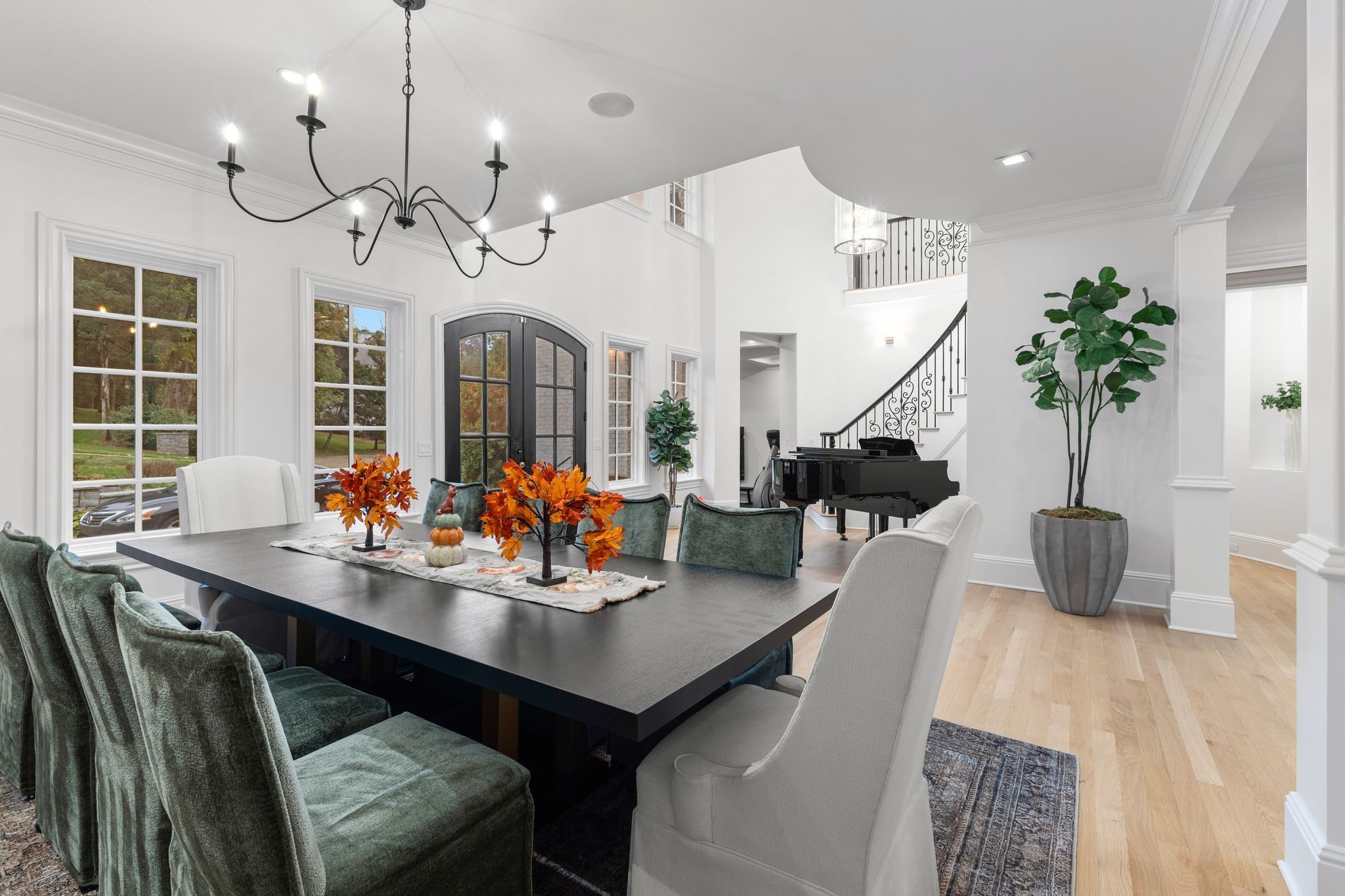 Dining room with a long dark table, arched glass doors, a grand piano, and curved staircase.