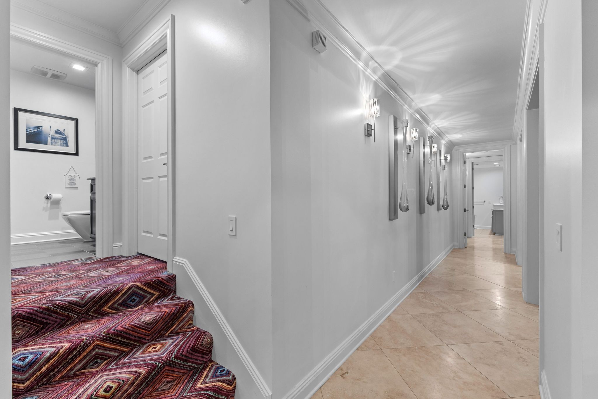 Hallway with tiled flooring, decorative sconces, and a staircase covered in colorful geometric carpet.