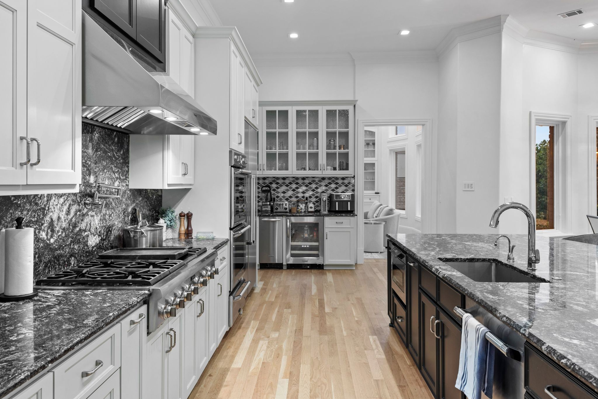 Kitchen with a large dark island, marble counters, white cabinetry, and stainless-steel appliances.