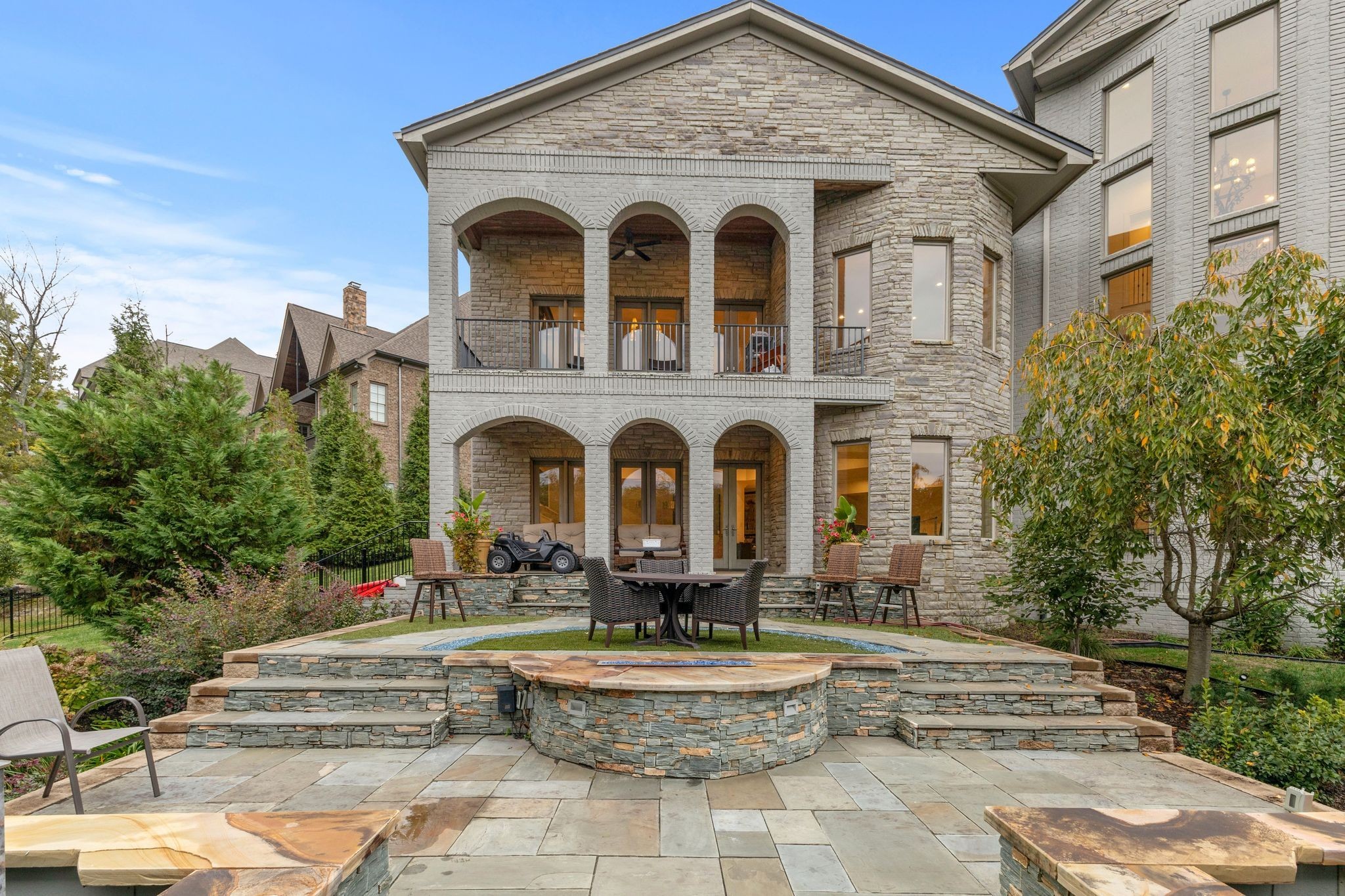 Stone home with two arched balconies above a tiered patio and central fire feature.
