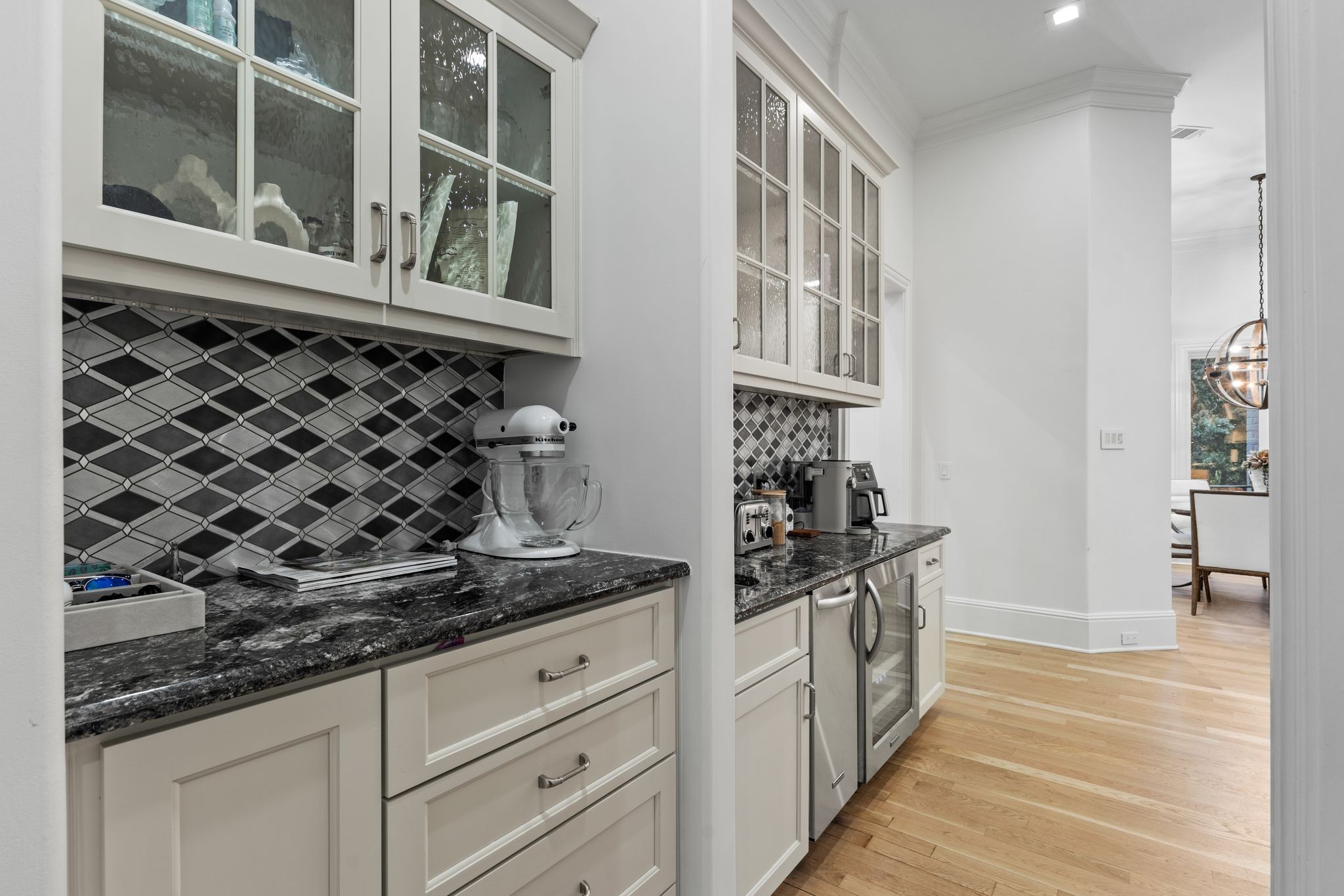 Butler’s pantry with geometric tile backsplash, dark granite counters, and glass-front cabinetry.