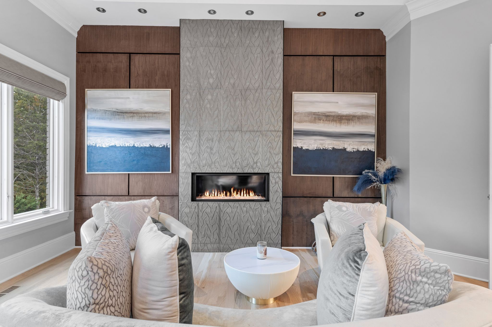 Staged living room with a gas fireplace, dark wood paneling, and two white chairs facing a round coffee table.