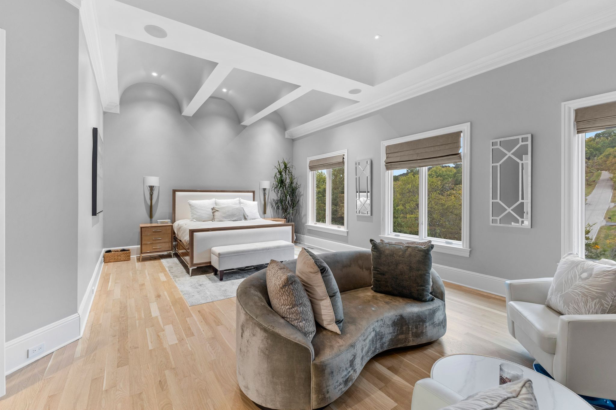 Staged bedroom with a sculpted tray ceiling, hardwood floors, and a curved sofa sitting area.
