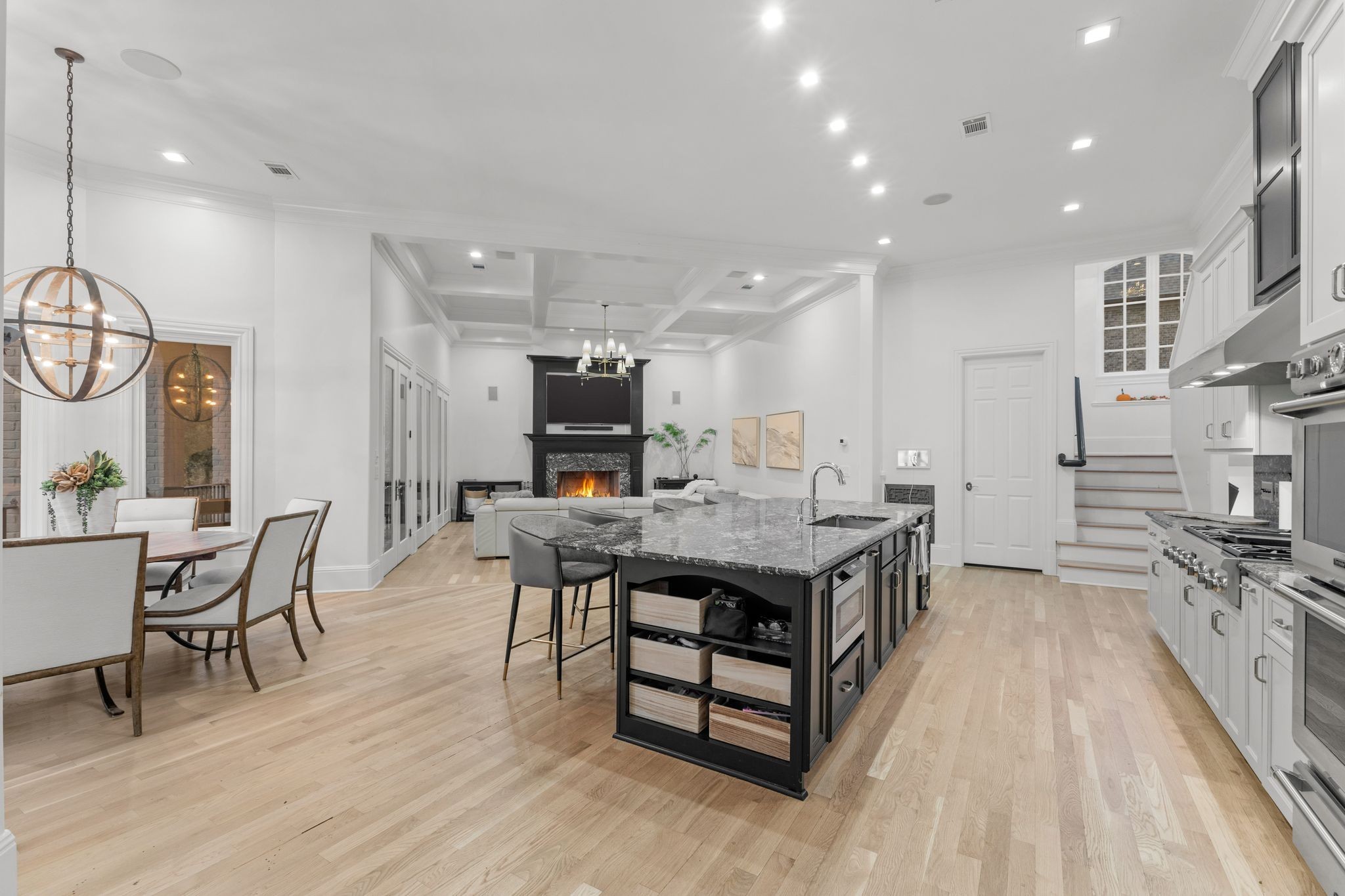 Open-plan kitchen with a large granite island, white cabinetry, and a fireplace beyond the dining area.