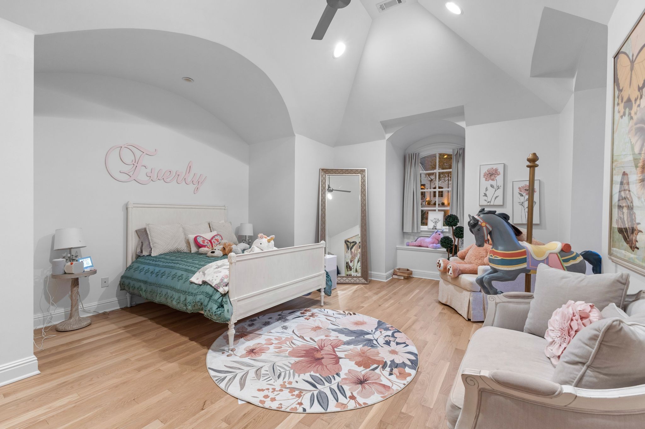 Furnished bedroom with a white bed, green bedding, plush toys, and a carousel horse.