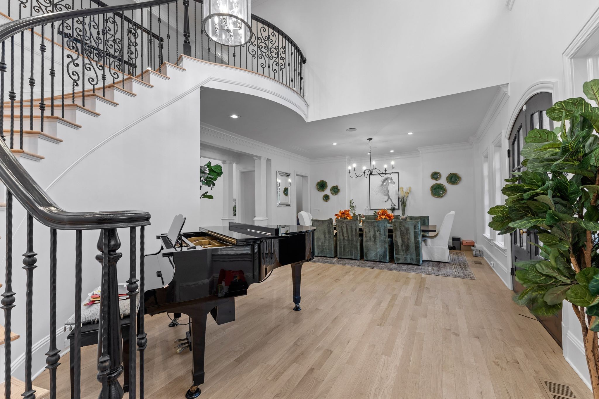 Open foyer with curved iron-railed staircase, black grand piano, and formal dining area.