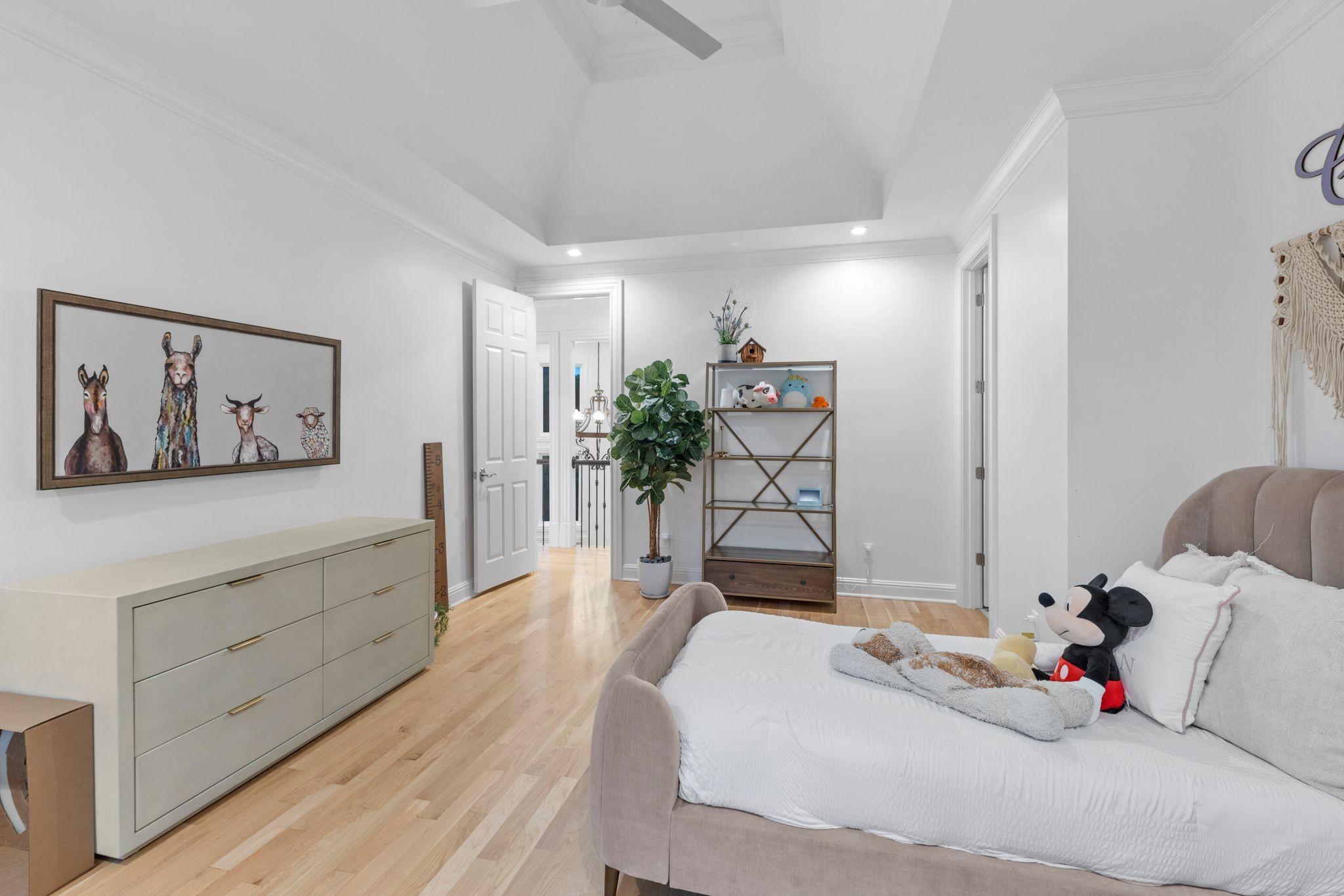 Furnished bedroom with a vaulted ceiling, light wood floors, and a pale upholstered bed.