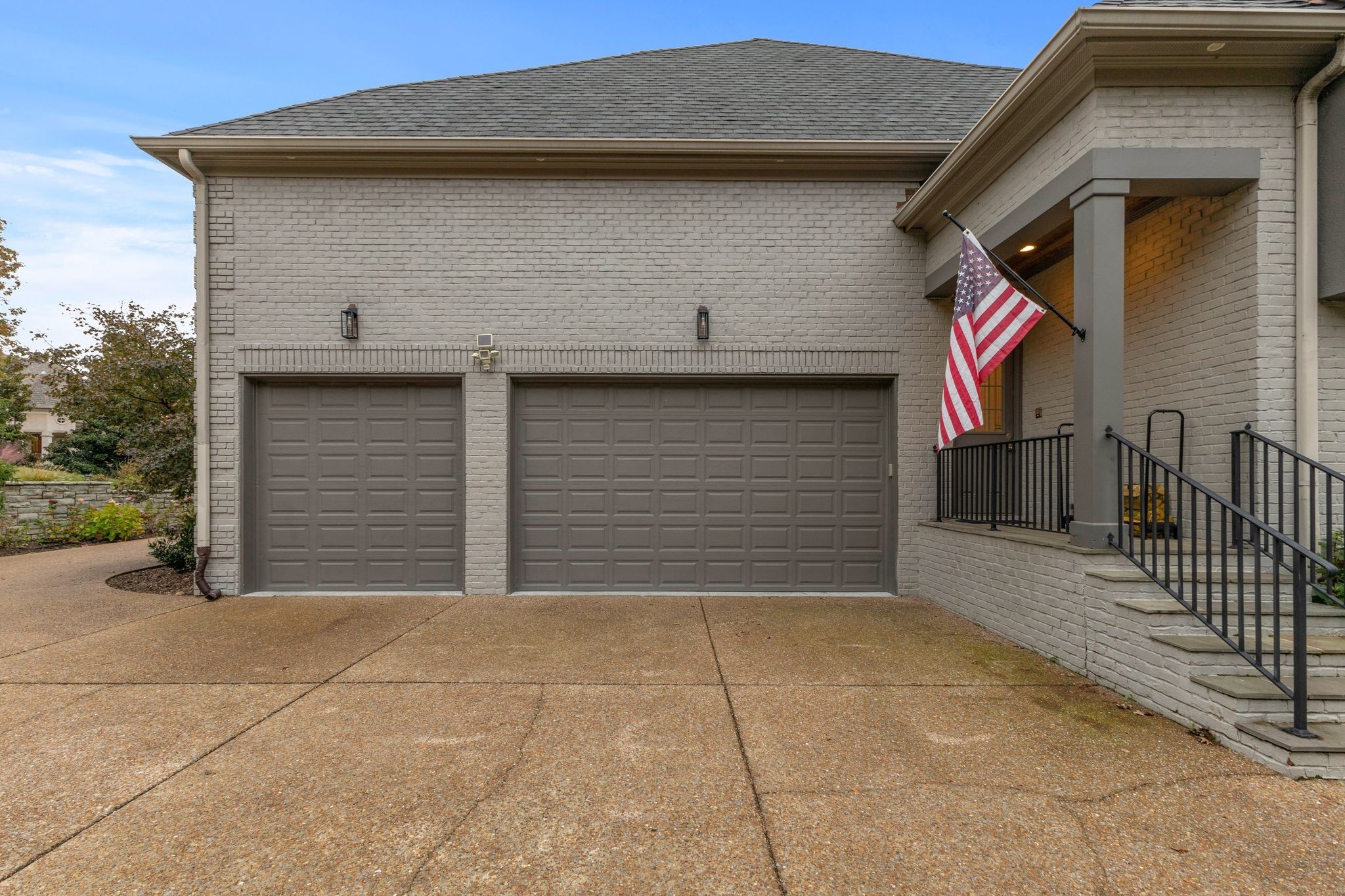 Brick home exterior with two garage doors, a broad driveway, and an American flag by the covered entry.
