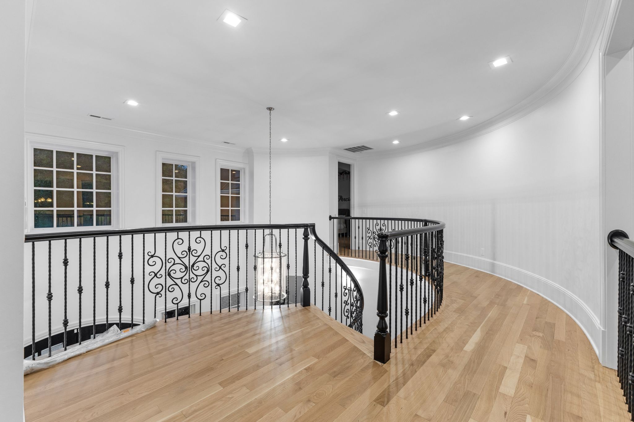 Upstairs landing with curved wrought-iron railings, a hanging glass lantern, and hardwood floors.