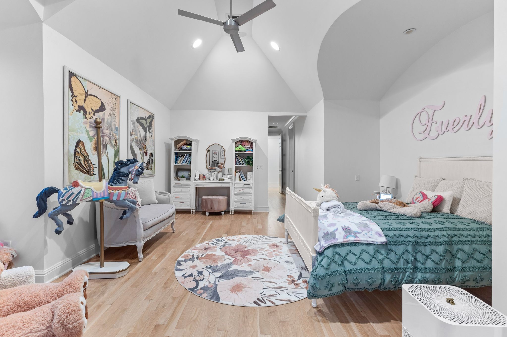 Child's bedroom with a teal bed, carousel horse, butterfly prints, and built-in vanity beneath a vaulted ceiling.