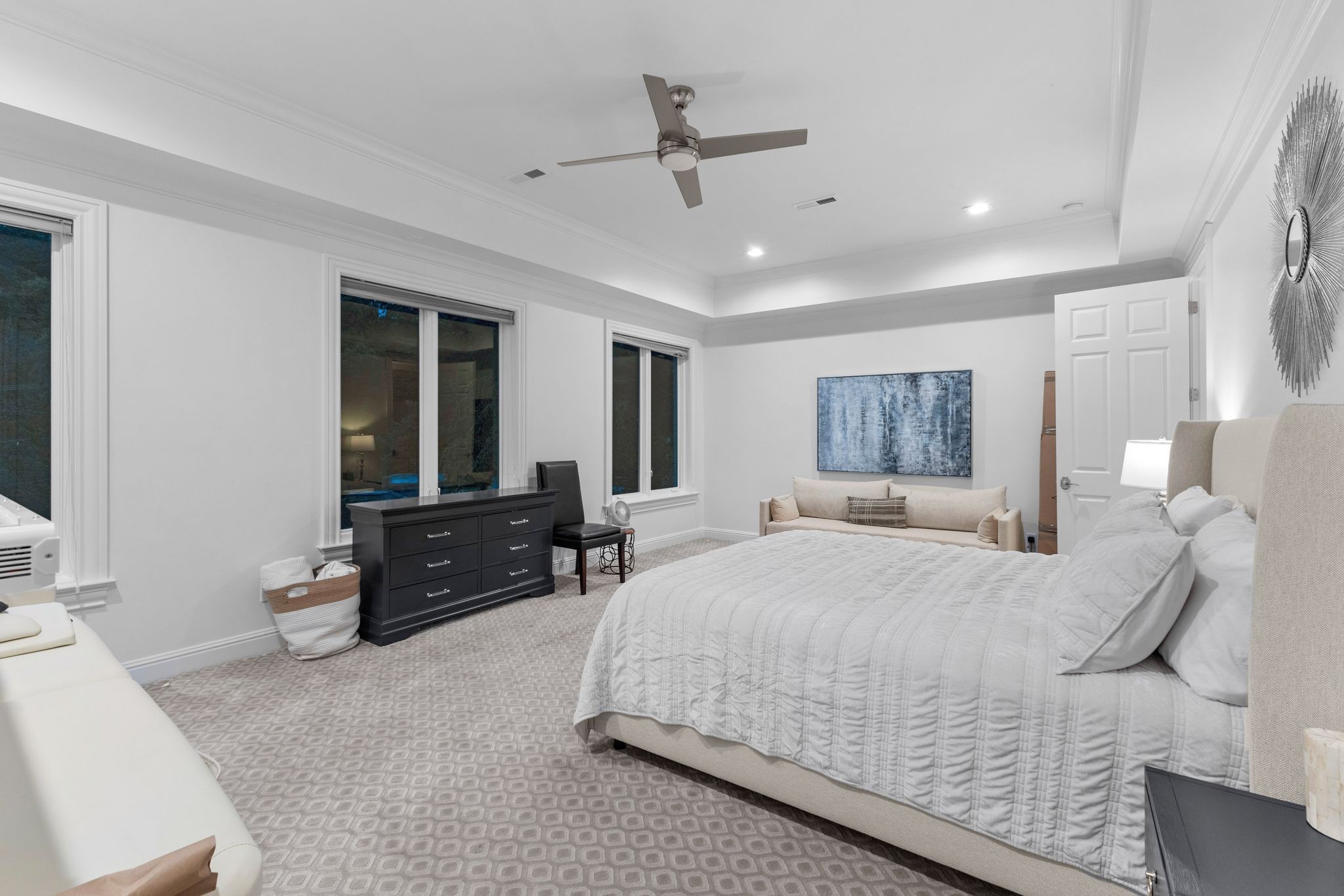 Furnished bedroom with a large bed, black dresser, small sofa, and ceiling fan.