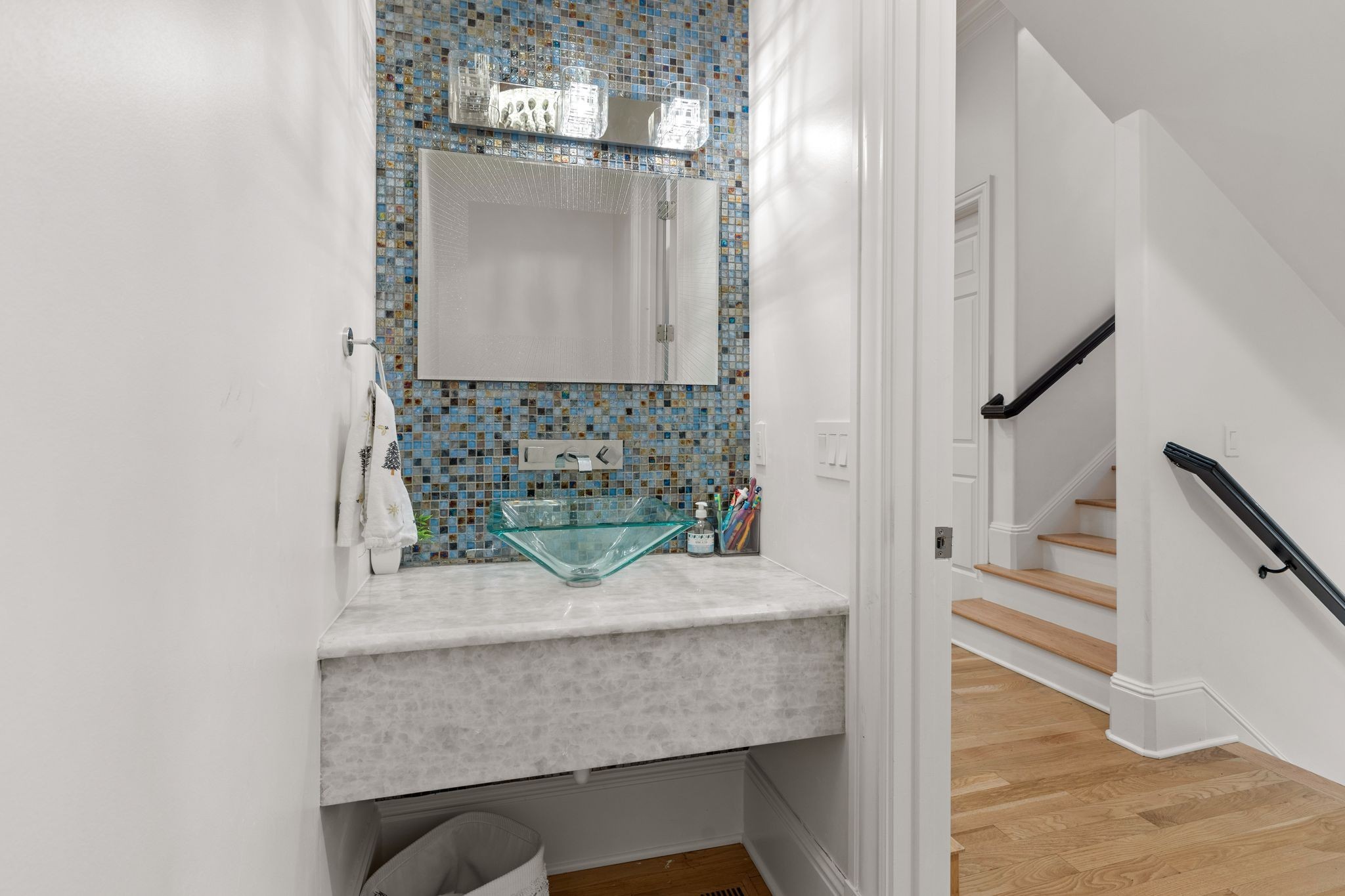 Bathroom vanity with a glass vessel sink and blue mosaic tile backsplash beside a wood staircase.