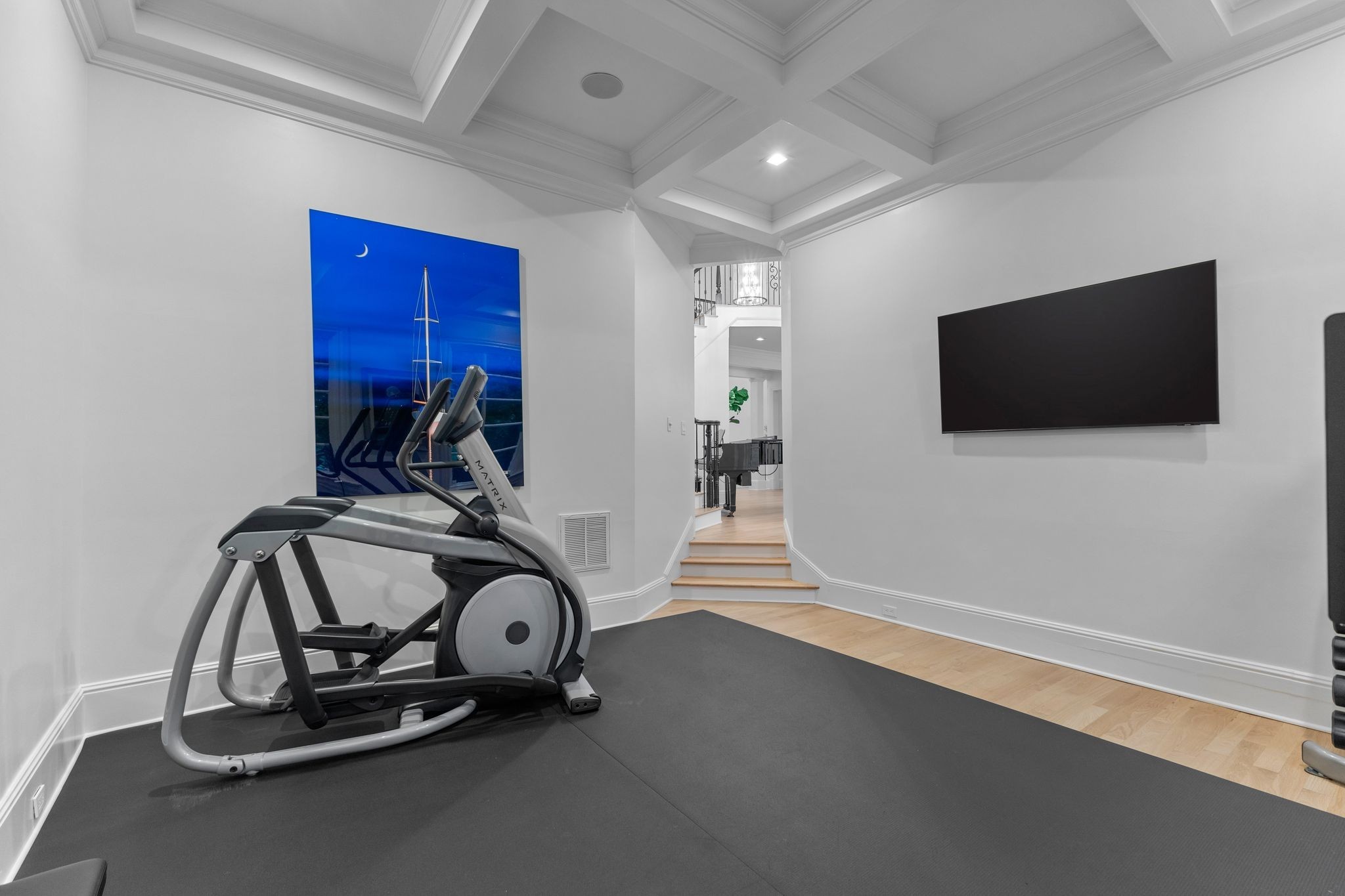 Home gym with an elliptical machine, wall-mounted television, and coffered ceiling.