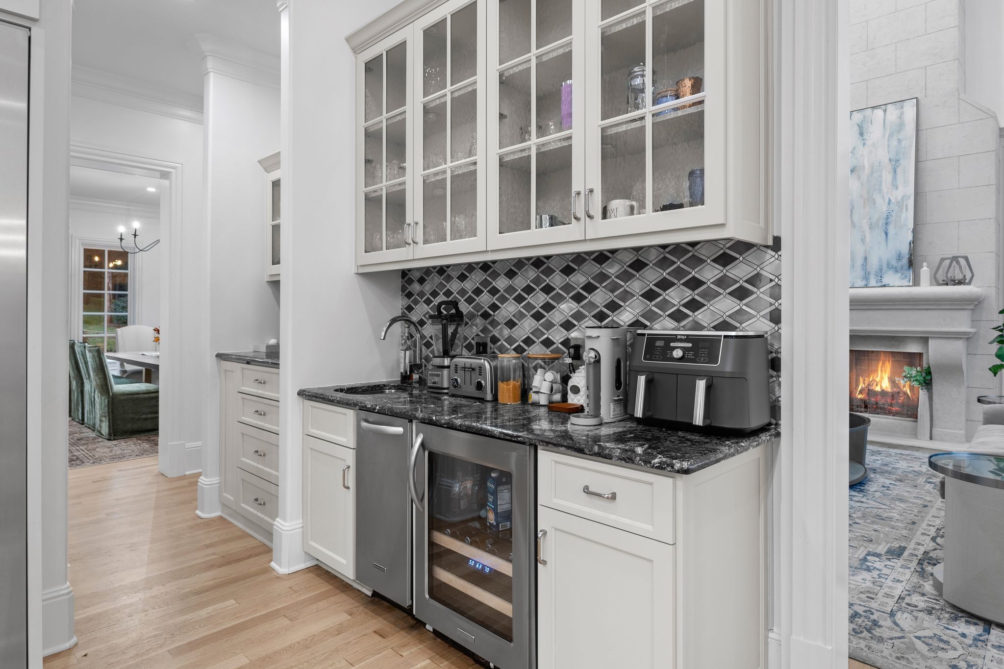 Kitchen beverage station with geometric tile backsplash, glass-front cabinets, and wine refrigerator.