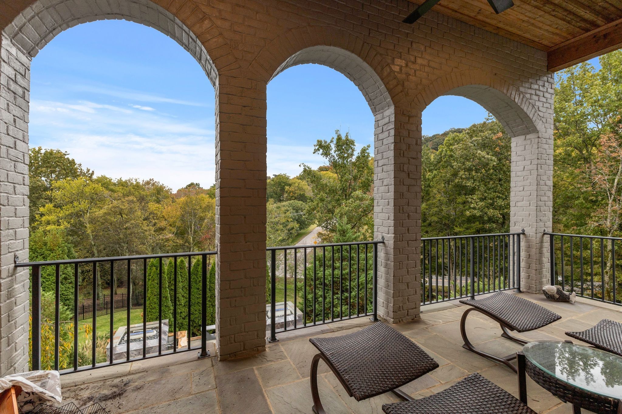 Covered terrace with arched brick openings and lounge chairs overlooking autumn trees.