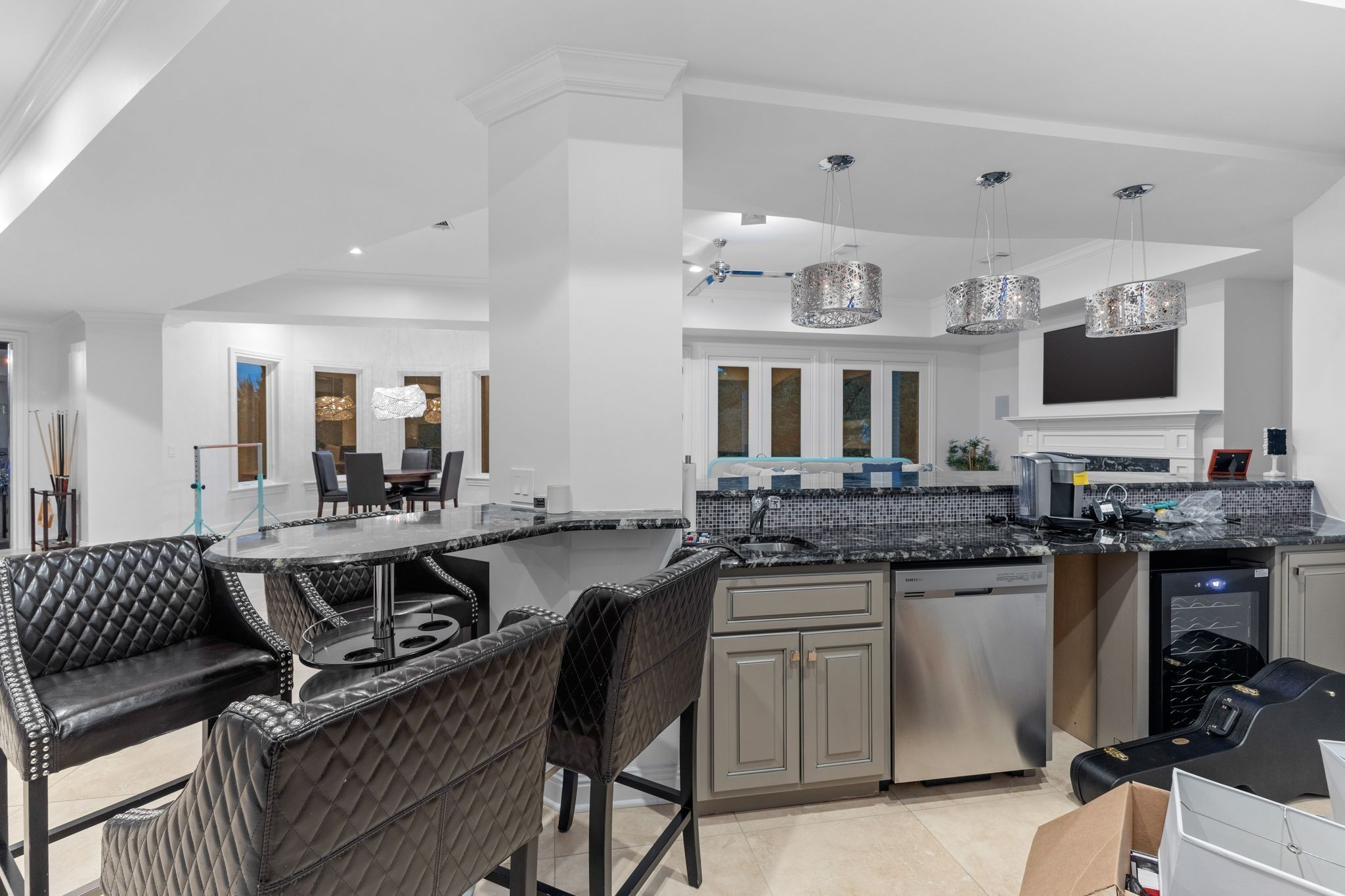 Open-plan kitchen with a curved marble island, quilted leather chairs, and three pendant lights.