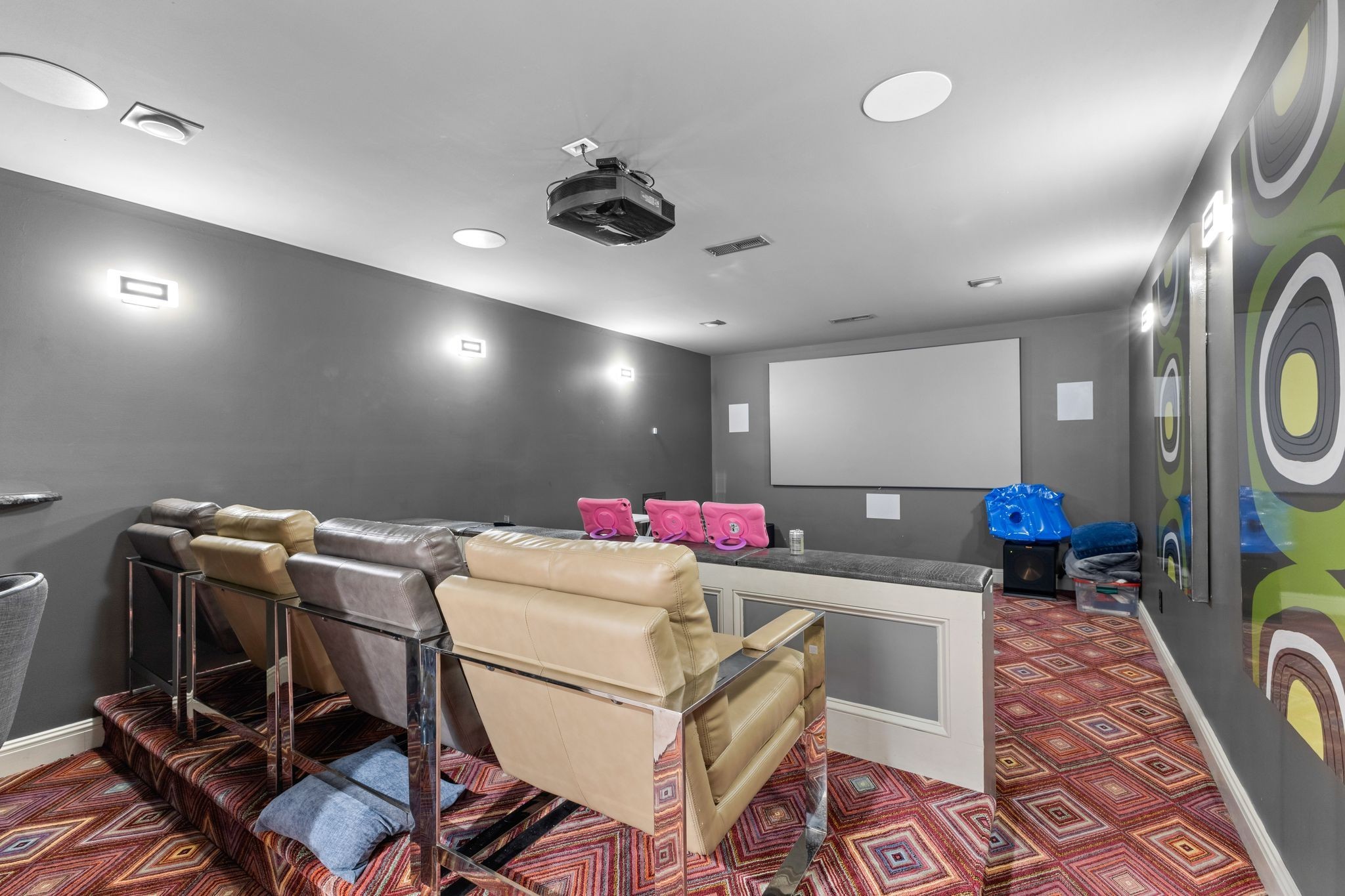 Furnished home theater with leather recliners, a large projection screen, and colorful geometric carpet.