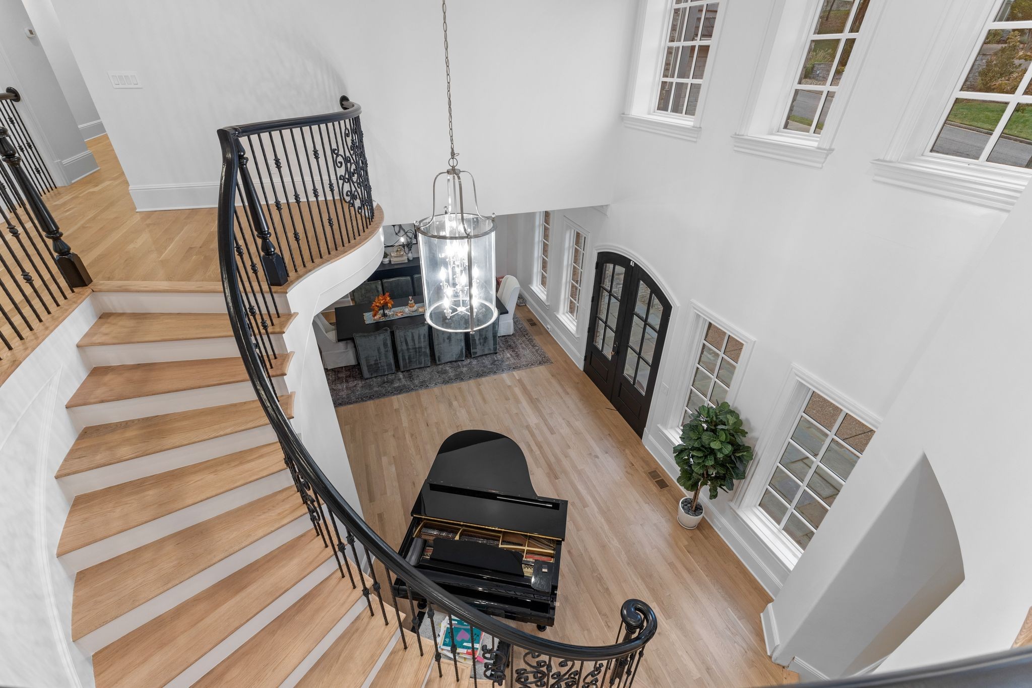 Two-story foyer with a curved wood staircase, black grand piano, tall windows, and glass chandelier.