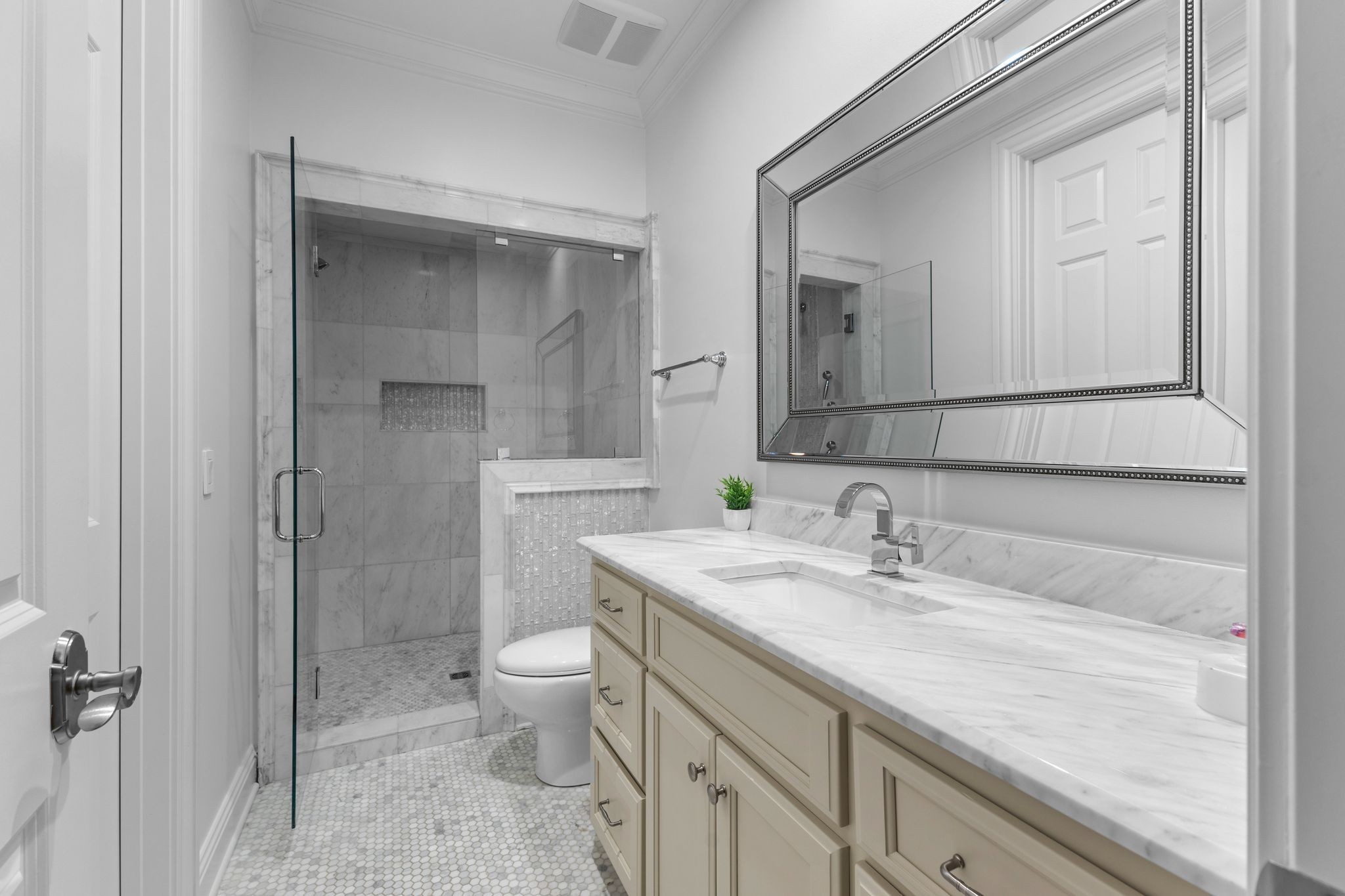 Bathroom with marble vanity and glass-enclosed marble shower.