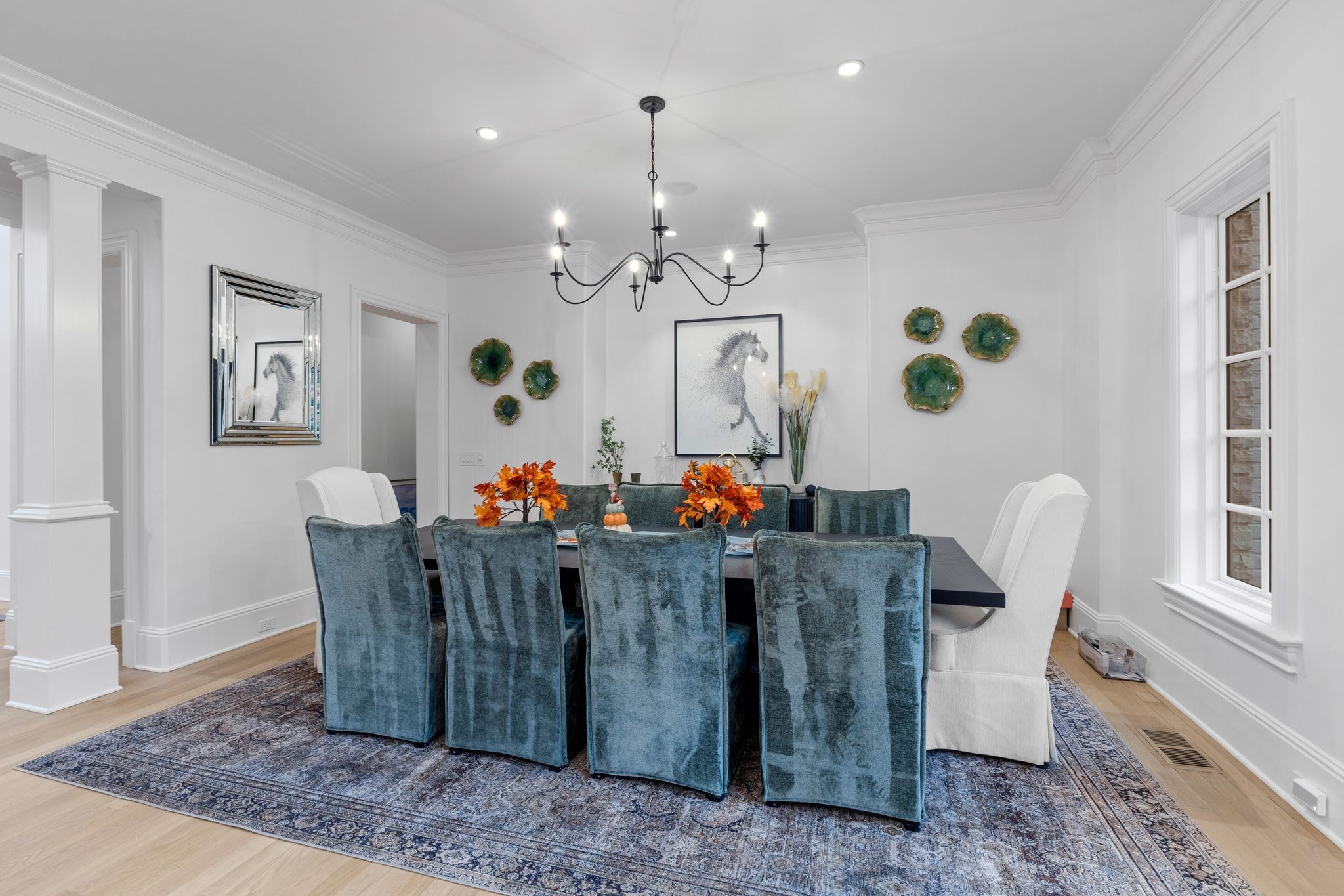 Dining room with blue velvet chairs, a dark table, black chandelier, and horse artwork.