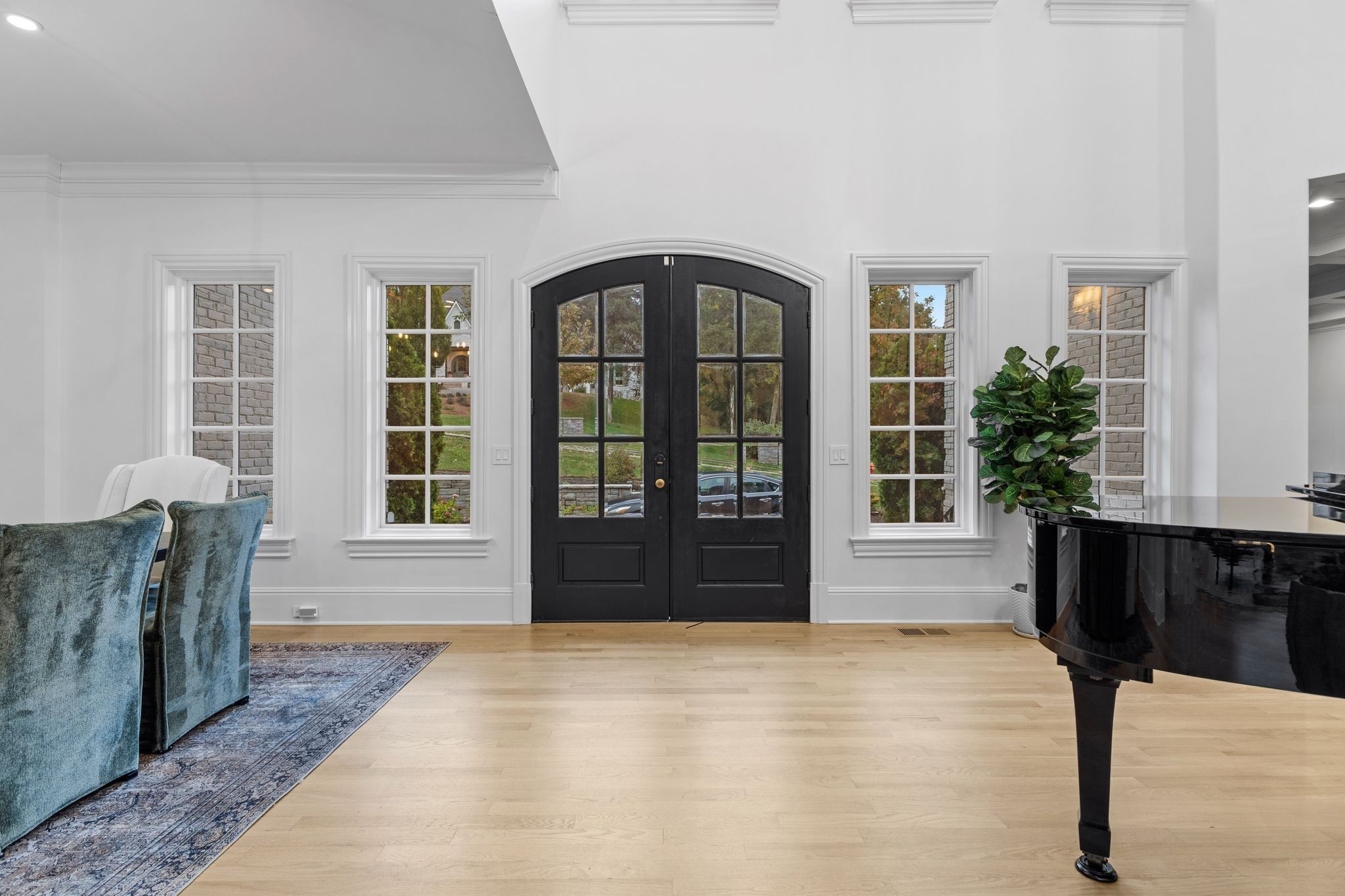 Entry hall with arched black double doors, pale hardwood floors, blue chairs, and a black grand piano.