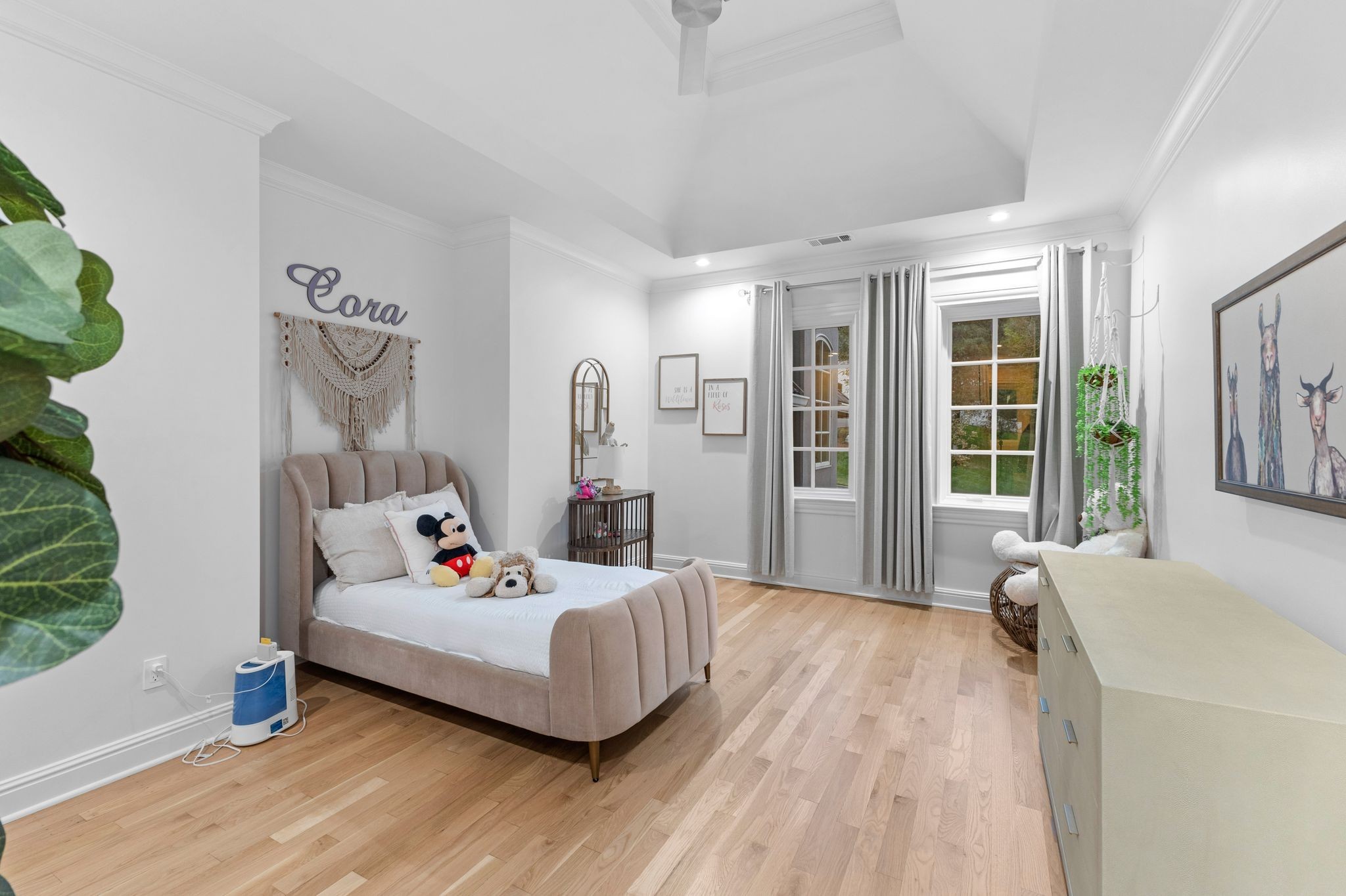 Child’s bedroom with a beige upholstered bed, stuffed toys, and the name Cora above it.